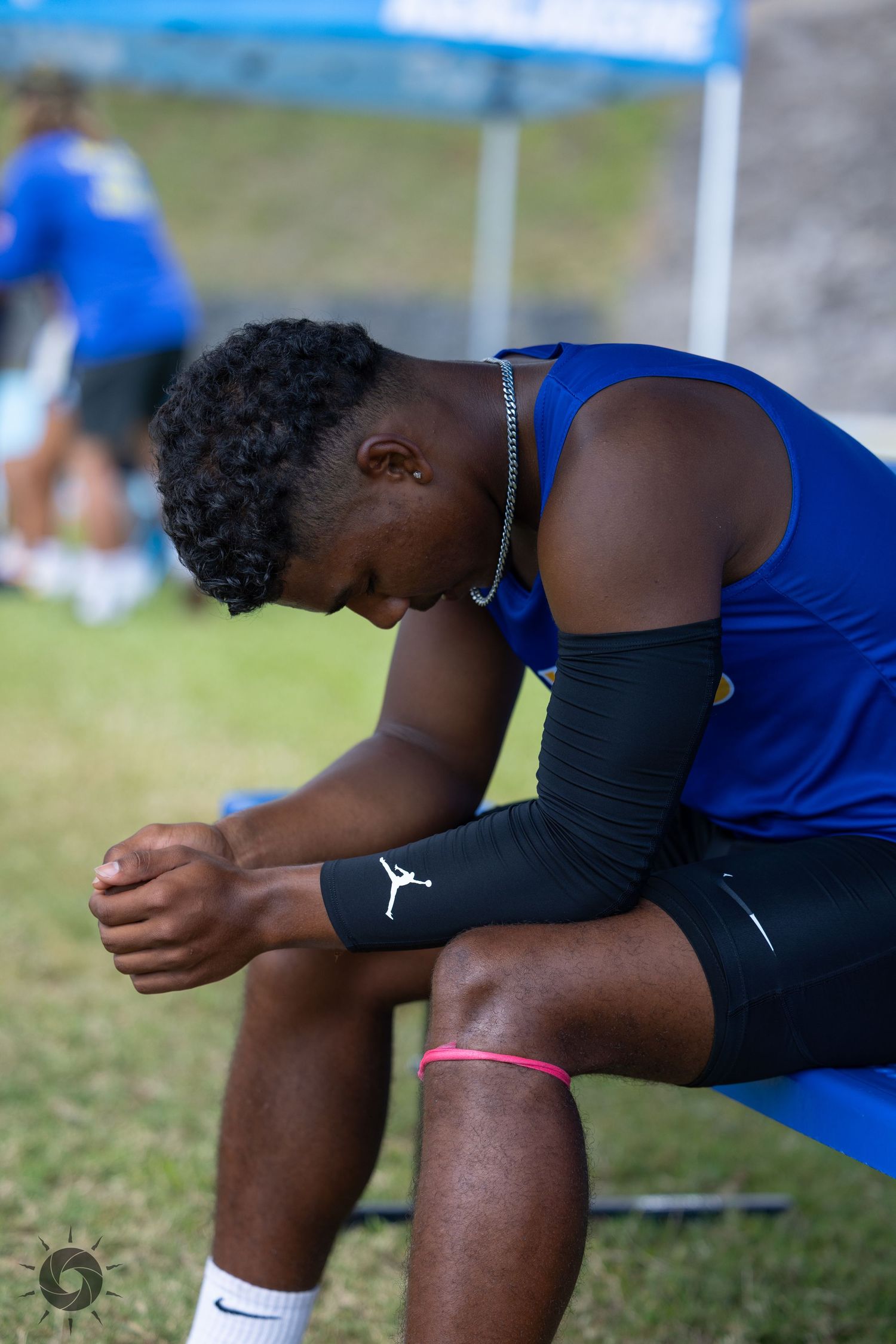 Athlete in blue uniform resting on the track with head down in a contemplative pose.