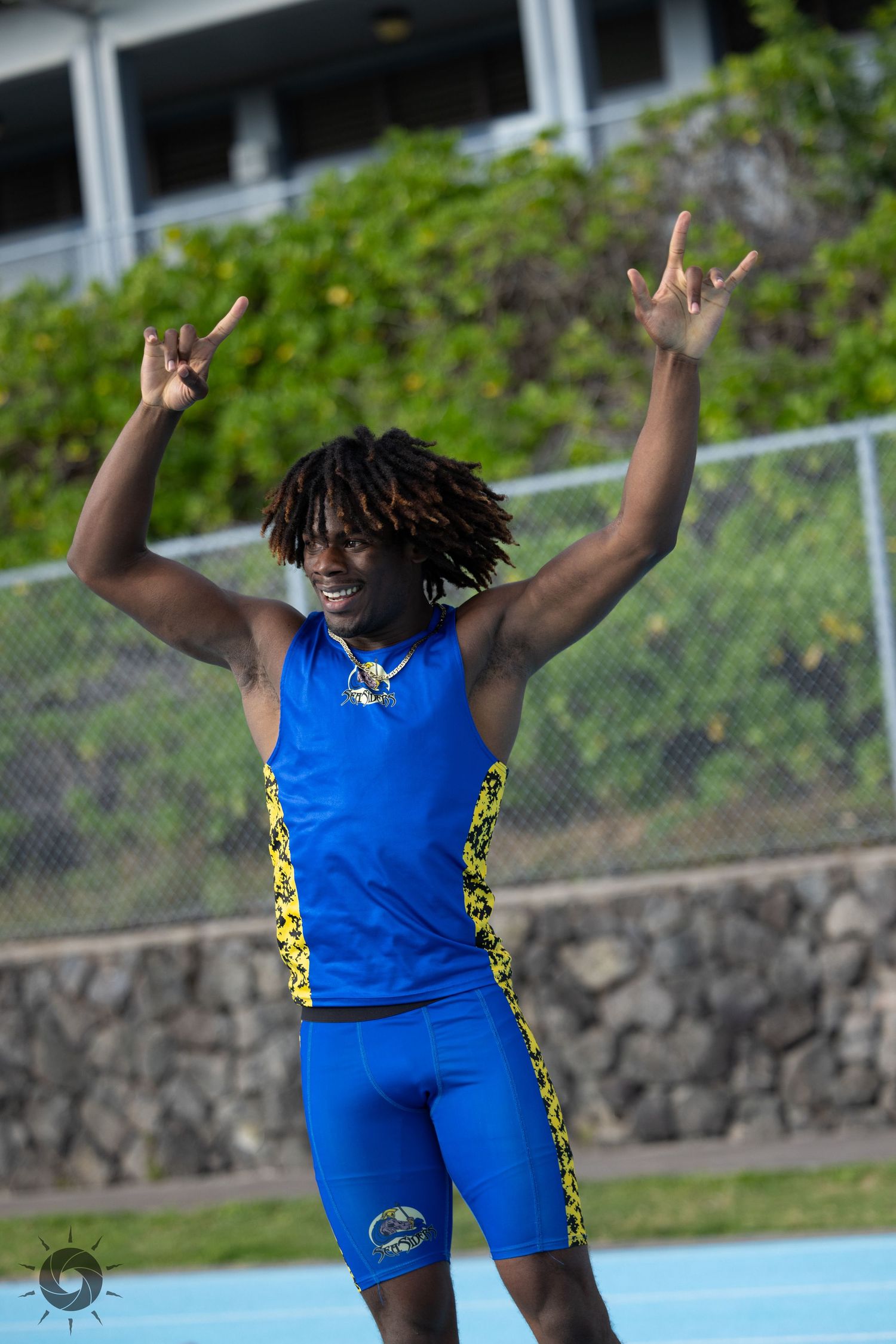 Athlete in bright blue and yellow track uniform celebrates with raised arms on a track field.