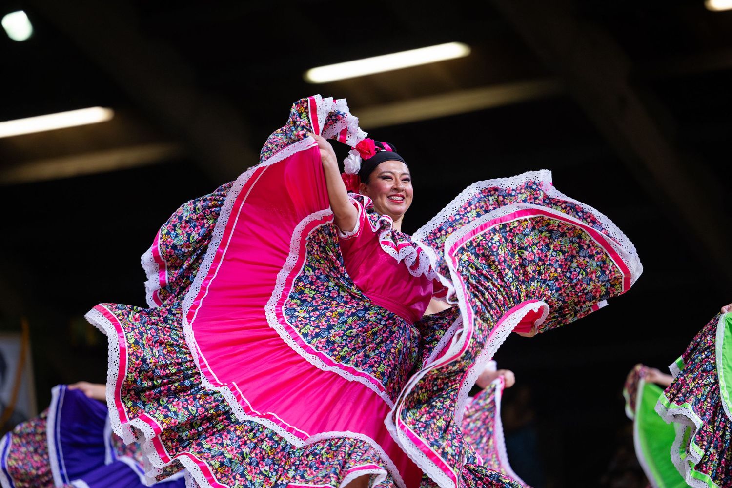 Dancers in vibrant pink and silver traditional Mexican folklorico dresses perform a synchronized twirling routine.