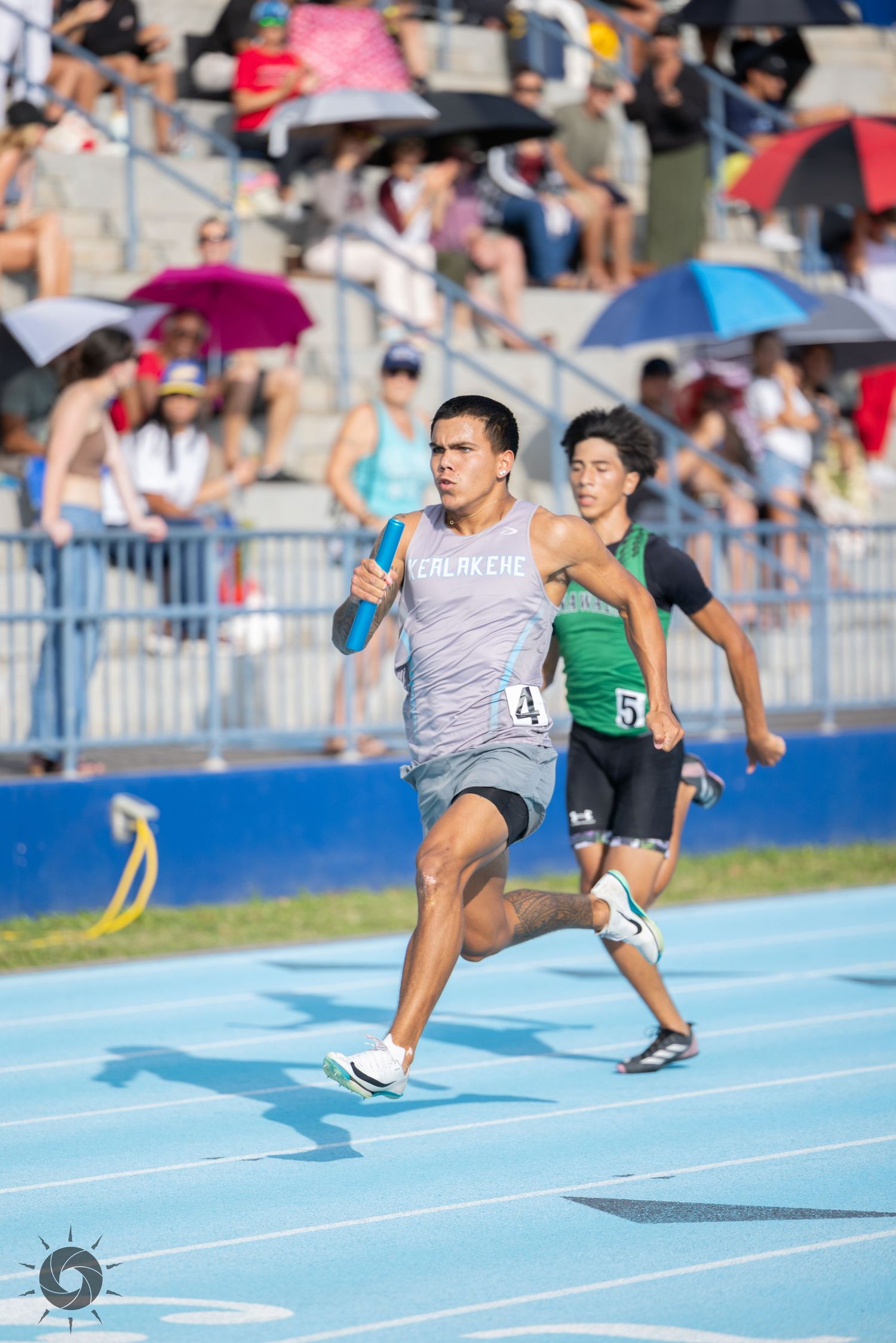 Athletes racing on blue track during competition with spectators watching in background.