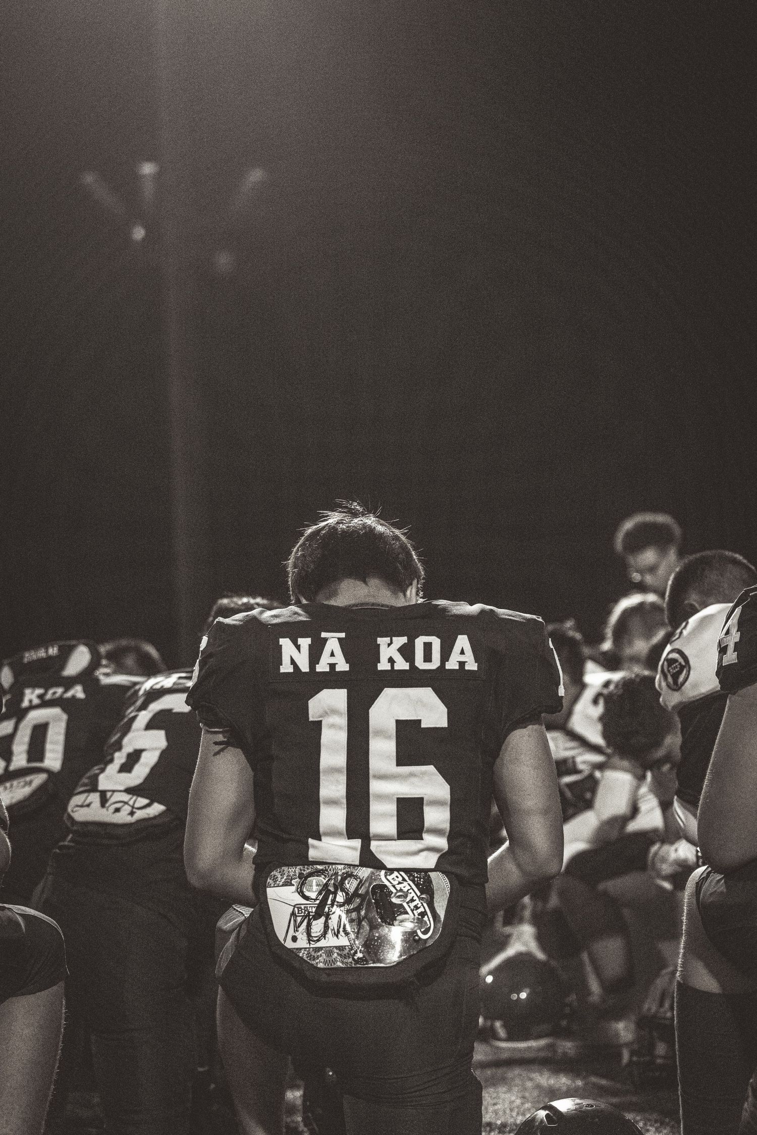 Row of performers in dark uniforms with 'NA KOA' visible on jerseys during a nighttime event.