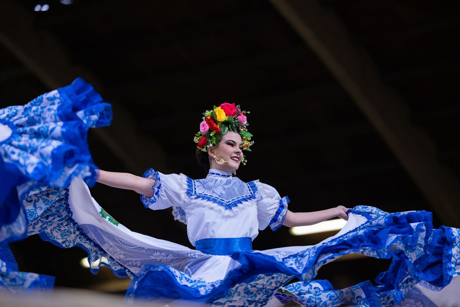 Dancers in flowing blue dresses perform graceful movements on a dark stage during a theatrical performance.