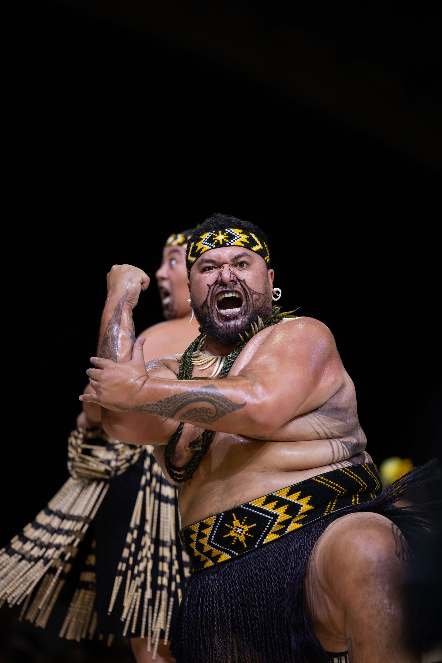 Traditional Maori warrior performing intense haka dance moves in dramatic lighting at cultural performance.