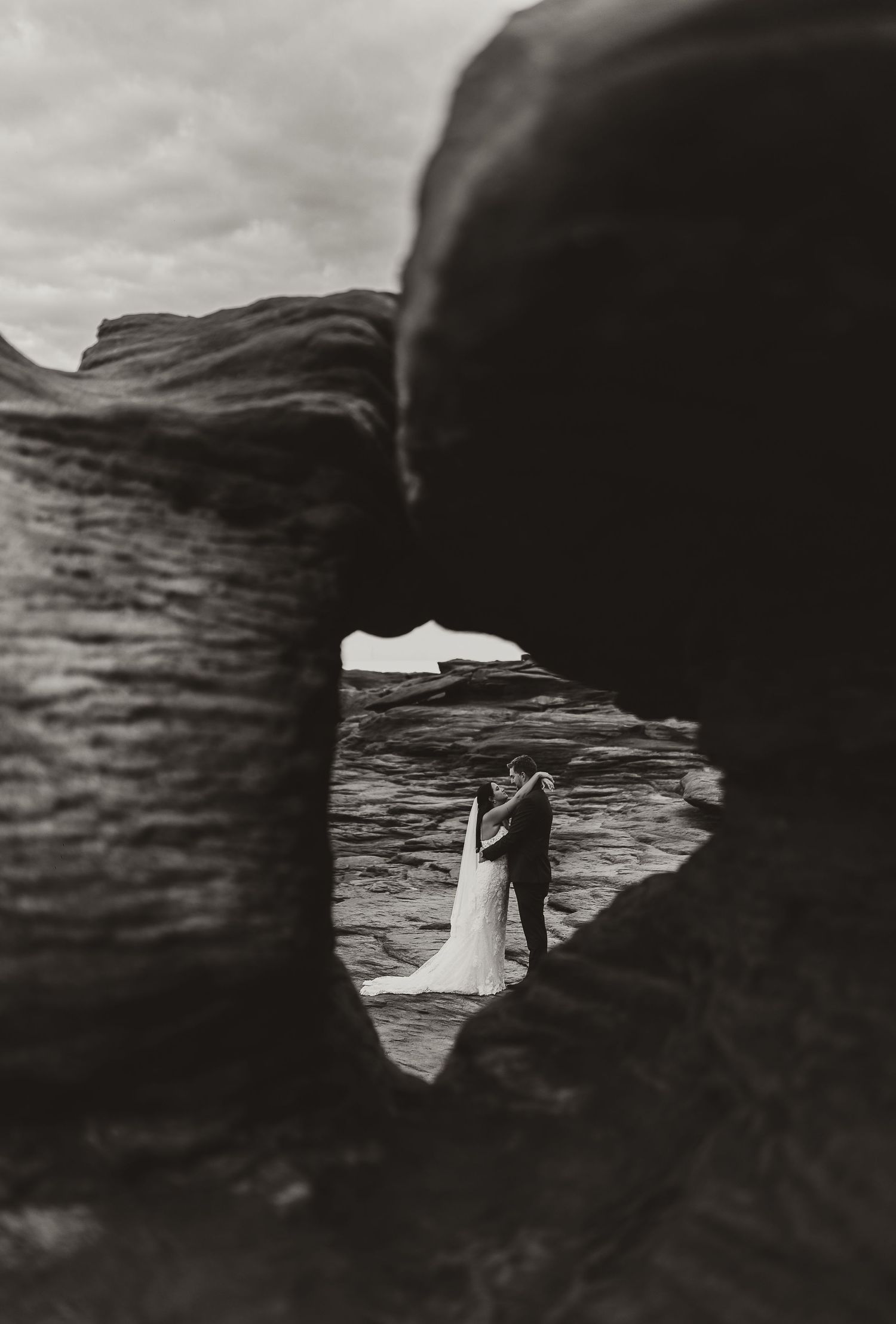 black and white image of bride and groom through a rock in cap pele