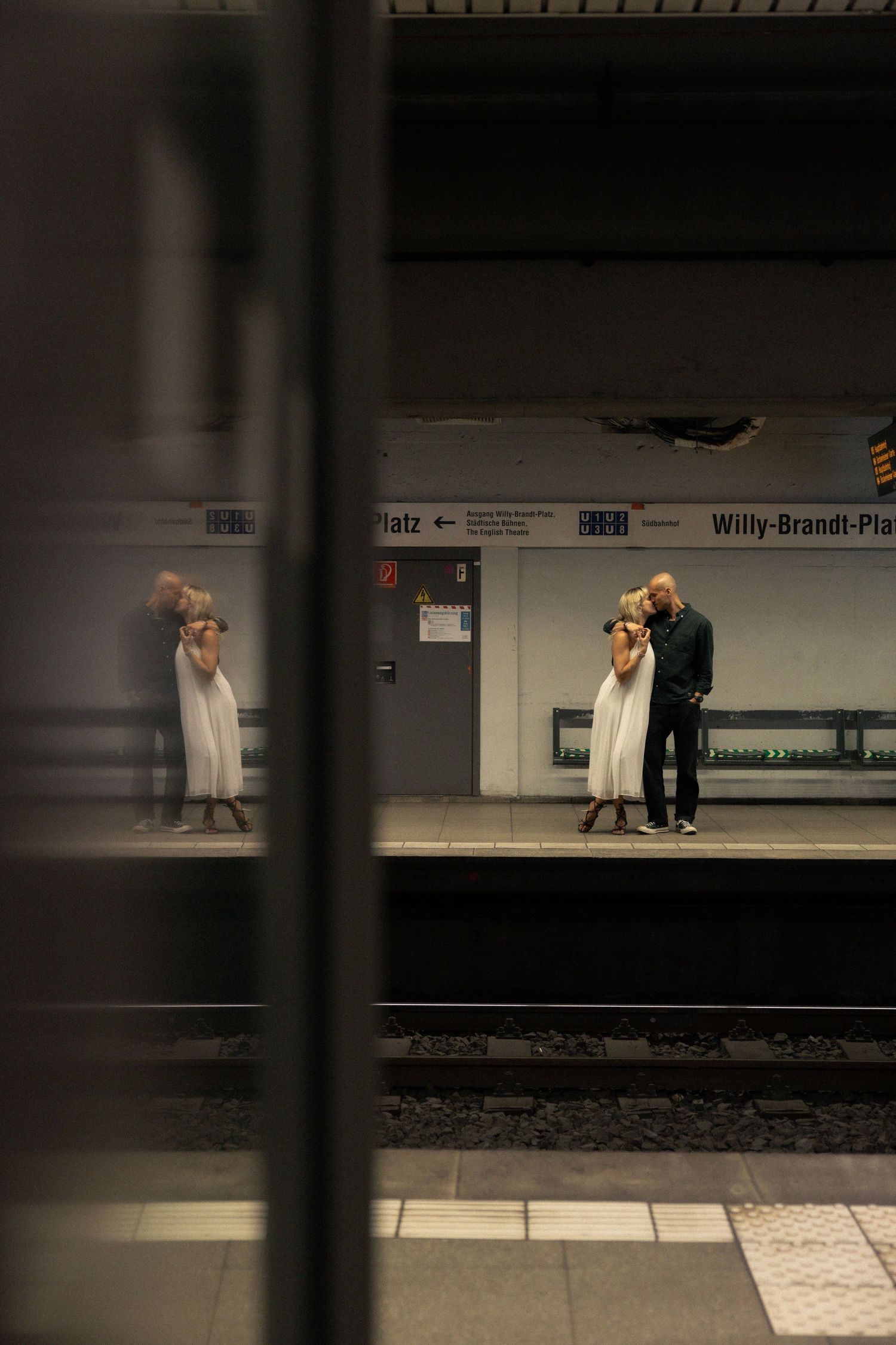 Couple embracing on opposite sides of a city train platform