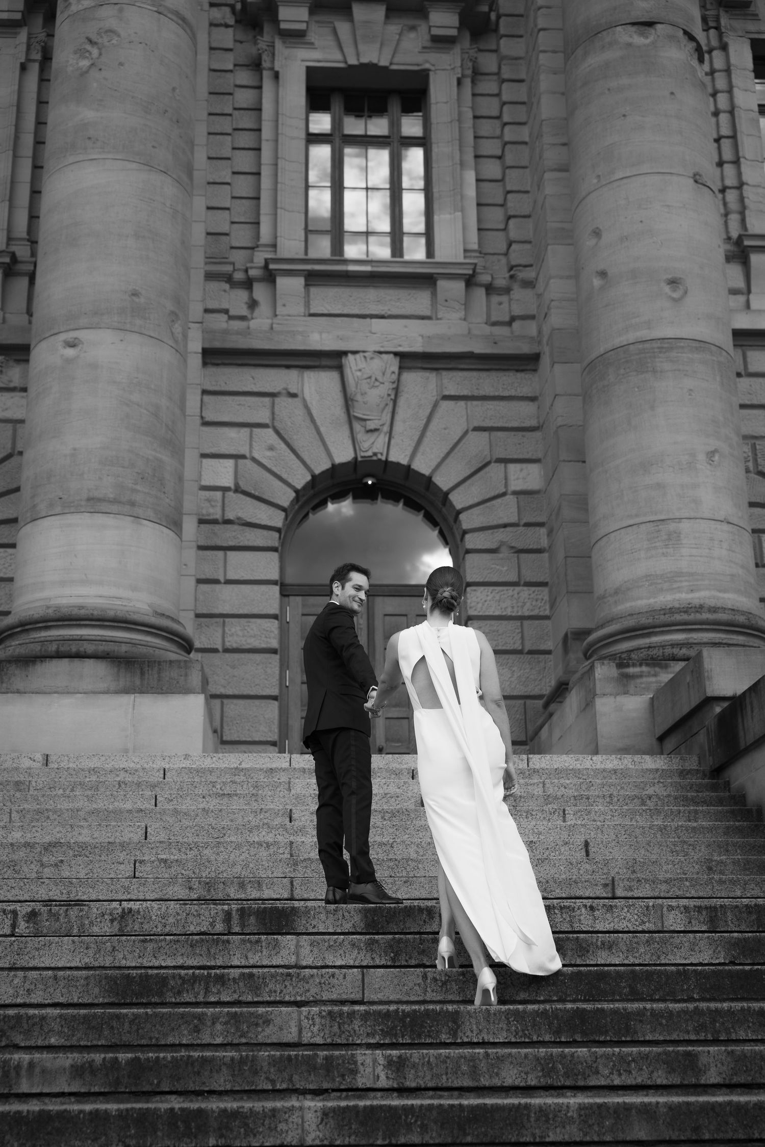 Newlyweds walking up grand stone steps in a black and white photograph