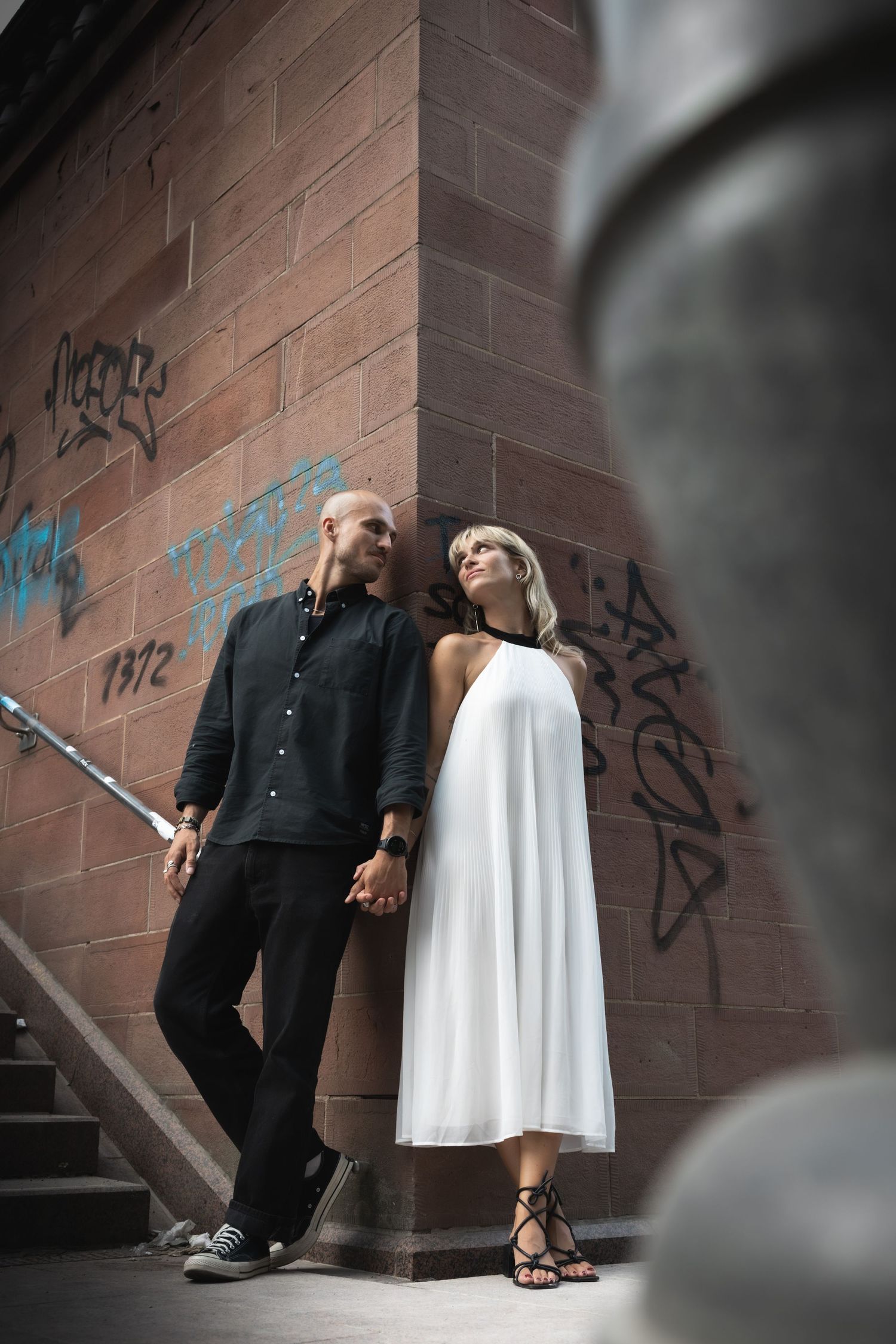 Couple holding hands beside a graffiti-covered brick wall