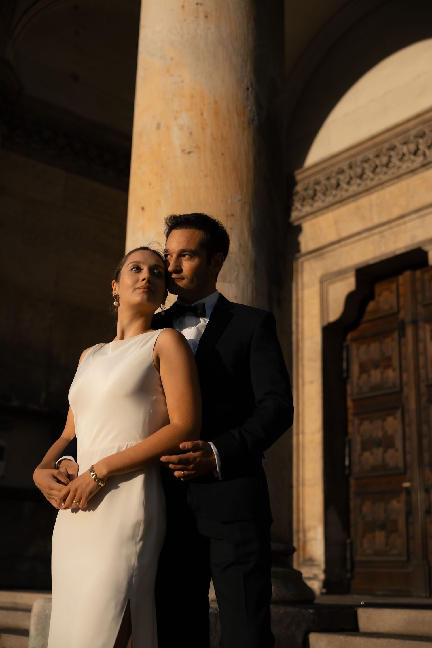 Newlyweds embracing beneath a grand stone column