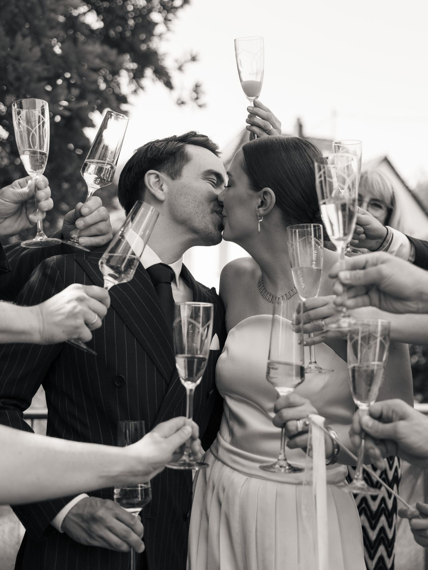 Newlyweds kissing as friends raise champagne glasses around them