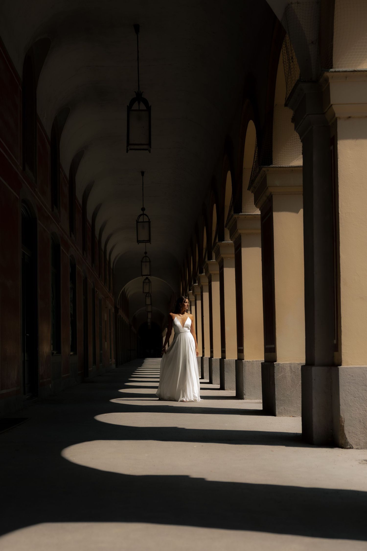 Bride standing alone in a grand sunlit corridor
