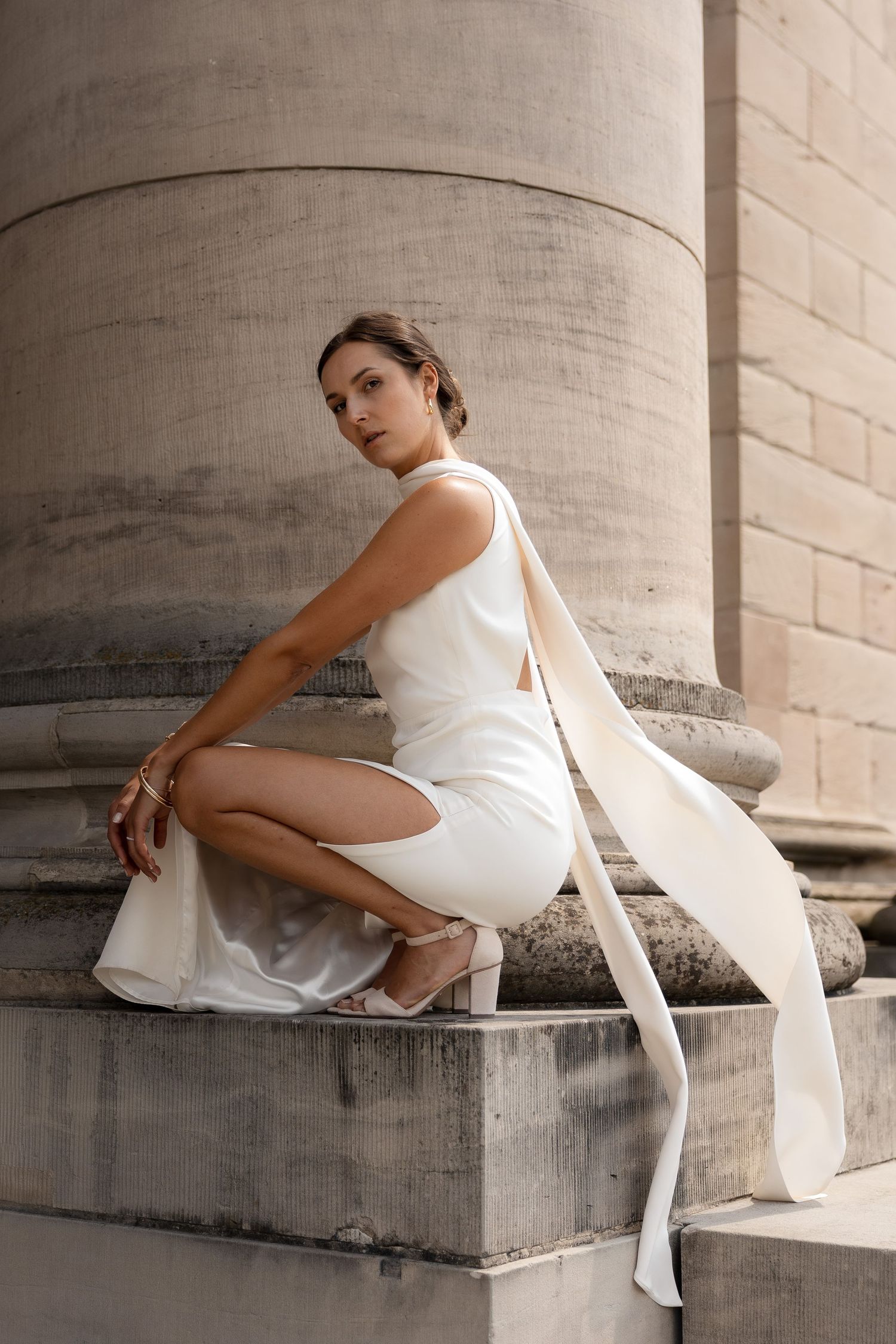 Bride sitting on steps wearing a white dress with a scarf that's flowing in the wind