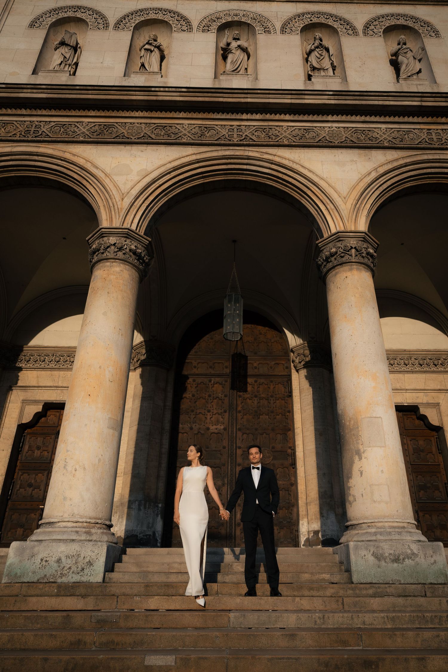 Newlyweds standing hand in hand up the steps of a historic building at sunset