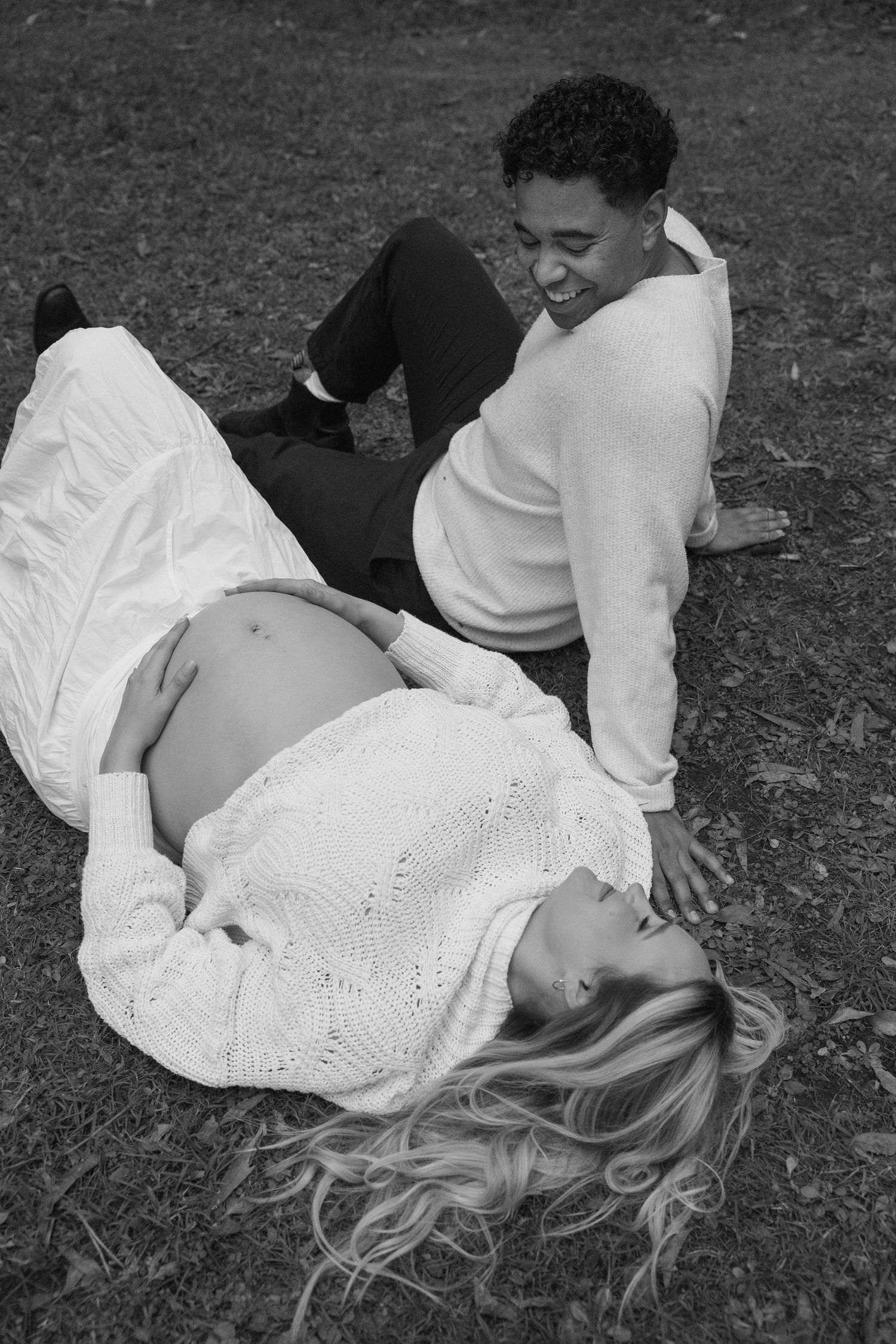 Pregnant couple lying together on the grass during an outdoor maternity session