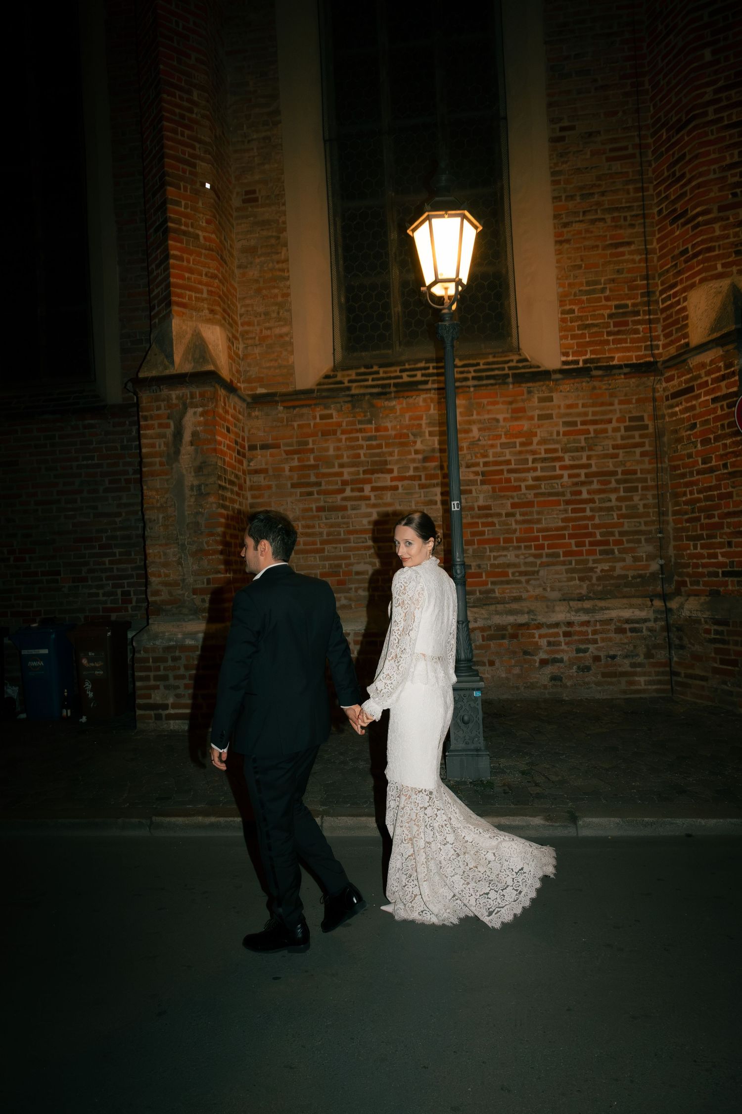 Newlyweds walking hand in hand through a city street at night