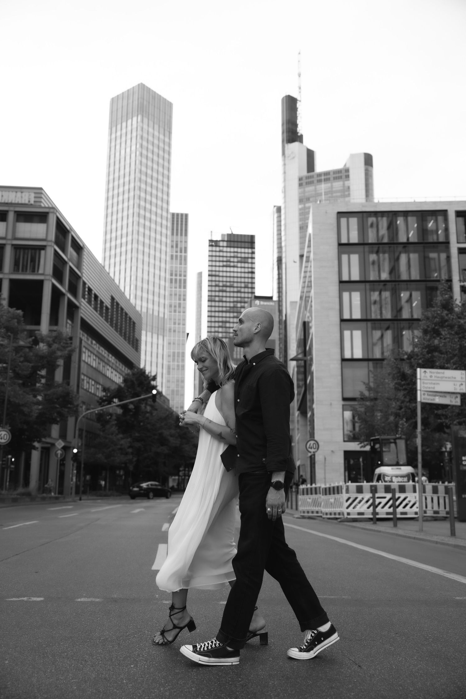 Couple walking over street in from of skyscrapers in black and white