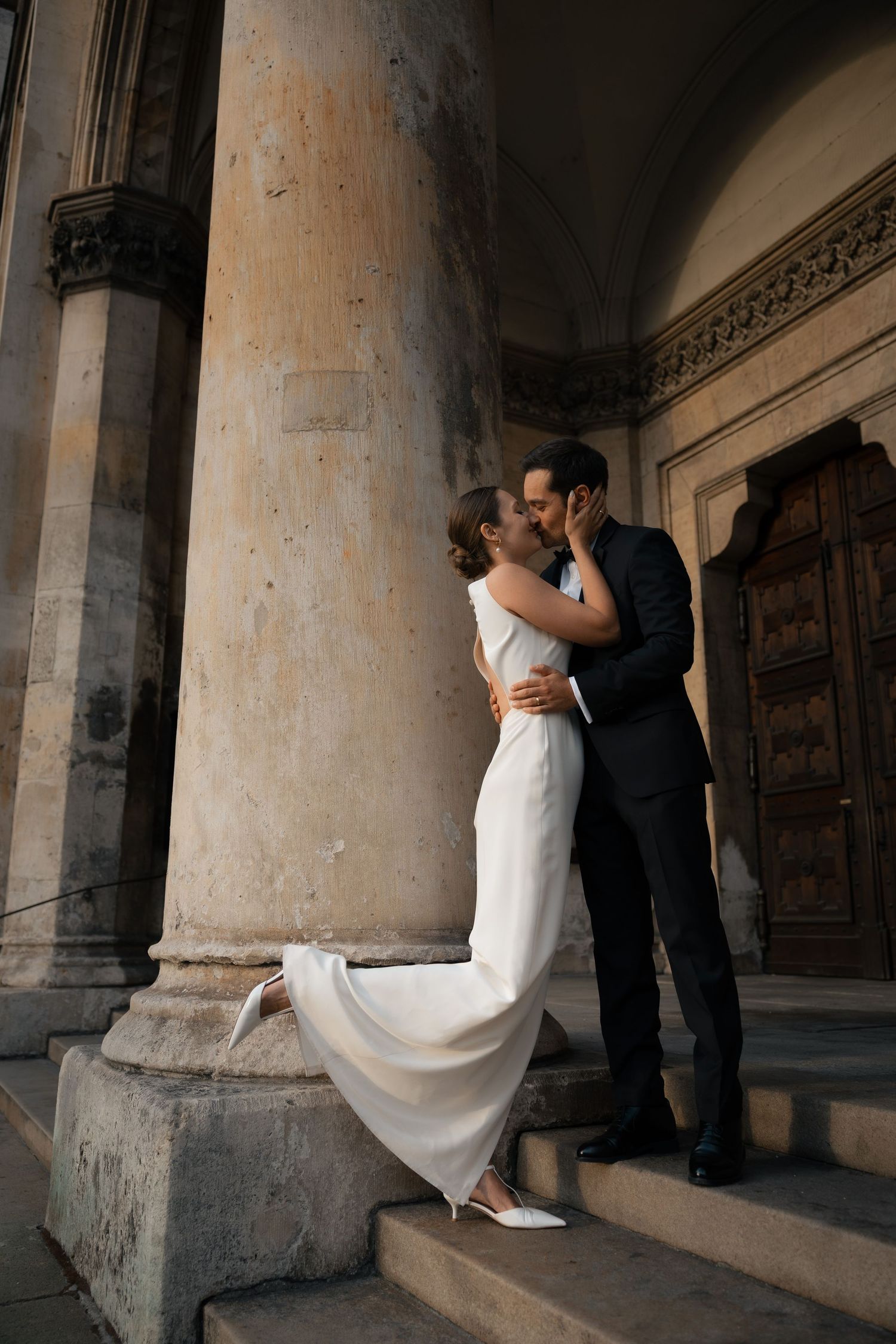 Newlyweds kissing beside a historic stone building