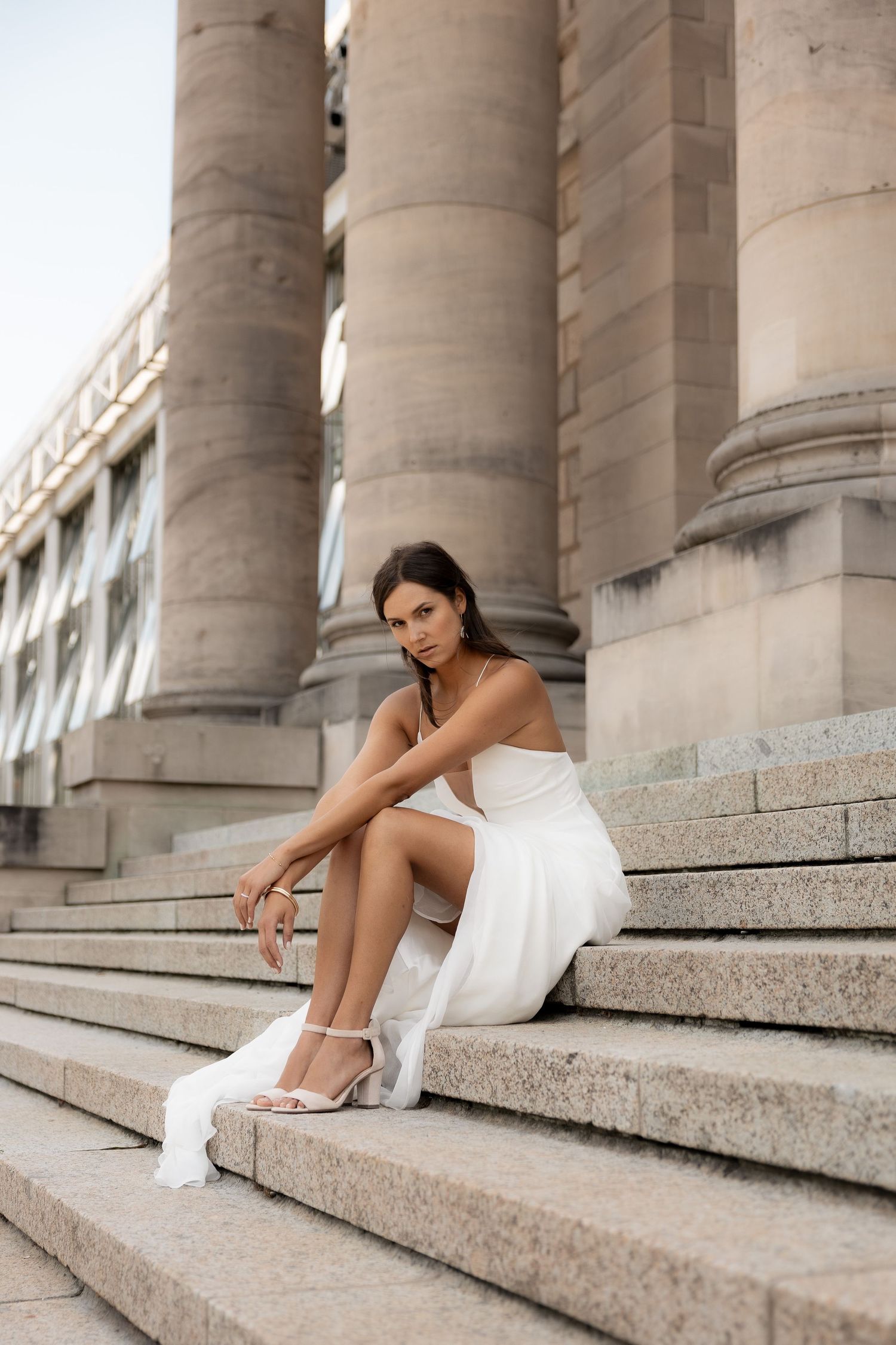 Bride sitting on stone steps in a flowing white wedding dress