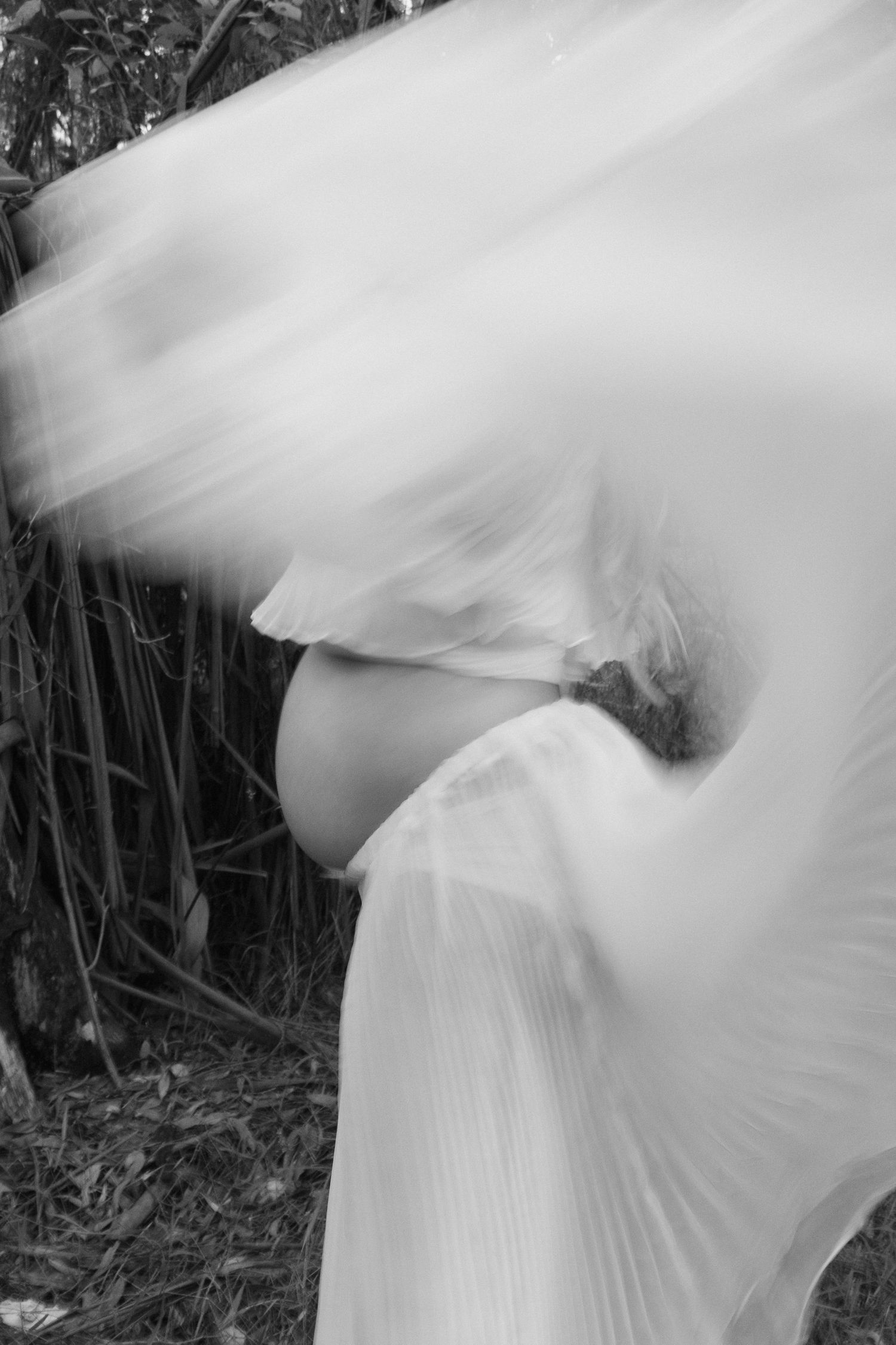 Pregnant couple embracing outdoors in a flowing white dress