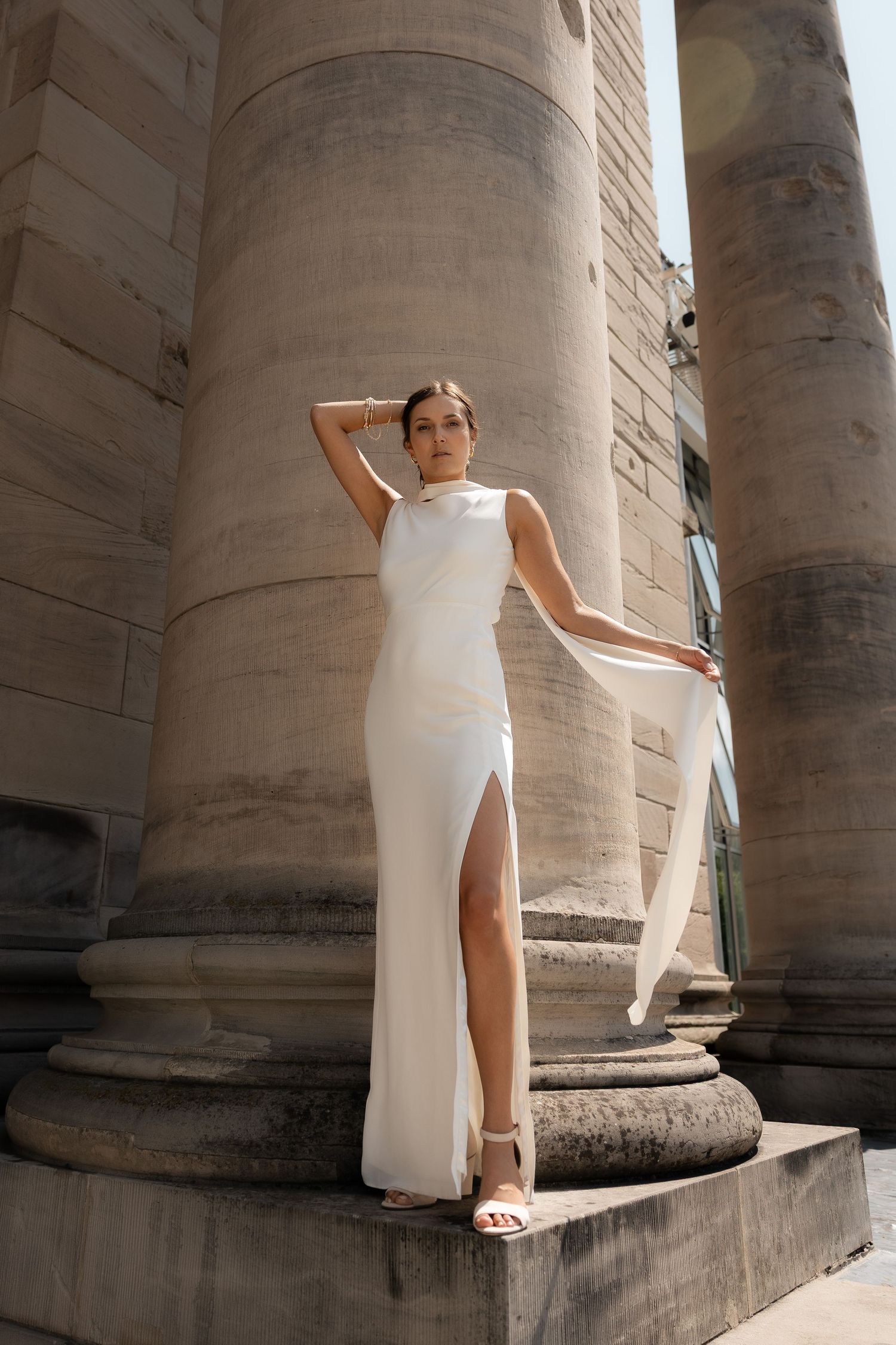 Bride posing on a historic stone column in a flowing white dress