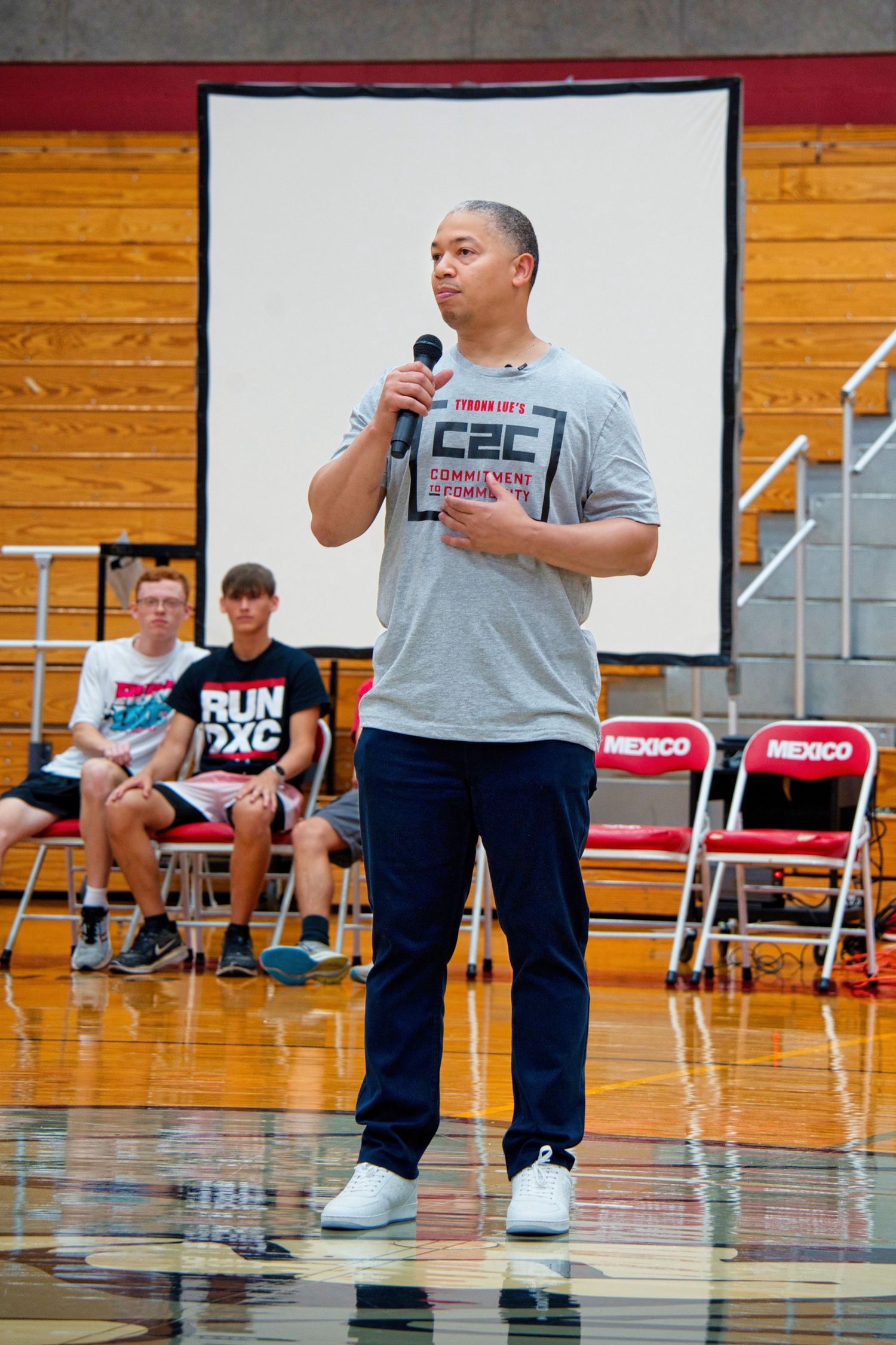 A man in a red shirt is speaking into a microphone on a stage.