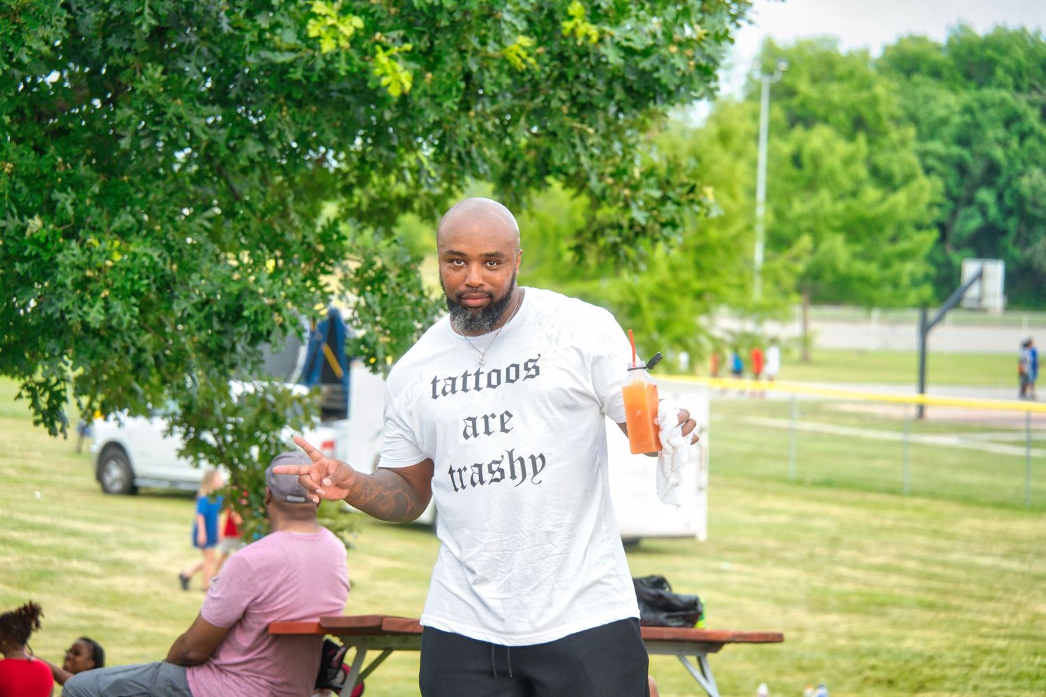 A man in a white shirt with the text 'Cutting the grass' is standing in a grassy area.