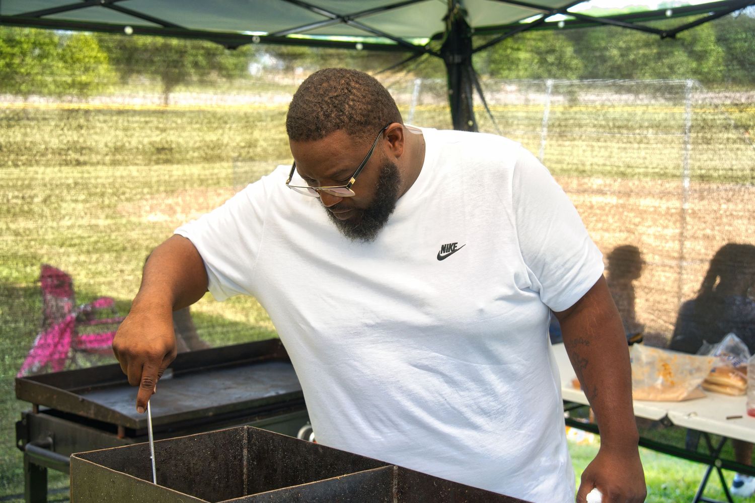 A man in a white shirt is standing in front of a grill and cooking something.
