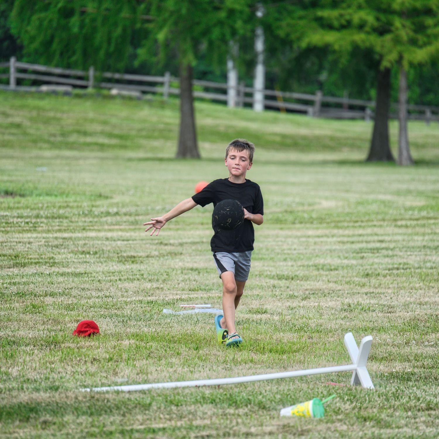 A young boy is running on a grassy field with playground equipment in the background.