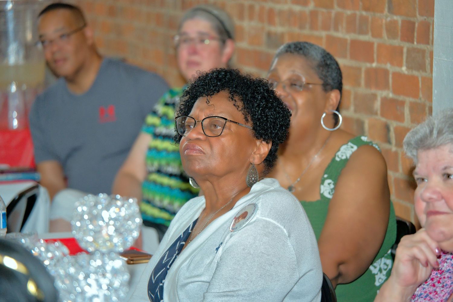 A group of people, including an older woman wearing a gray shirt, are gathered together and smiling.