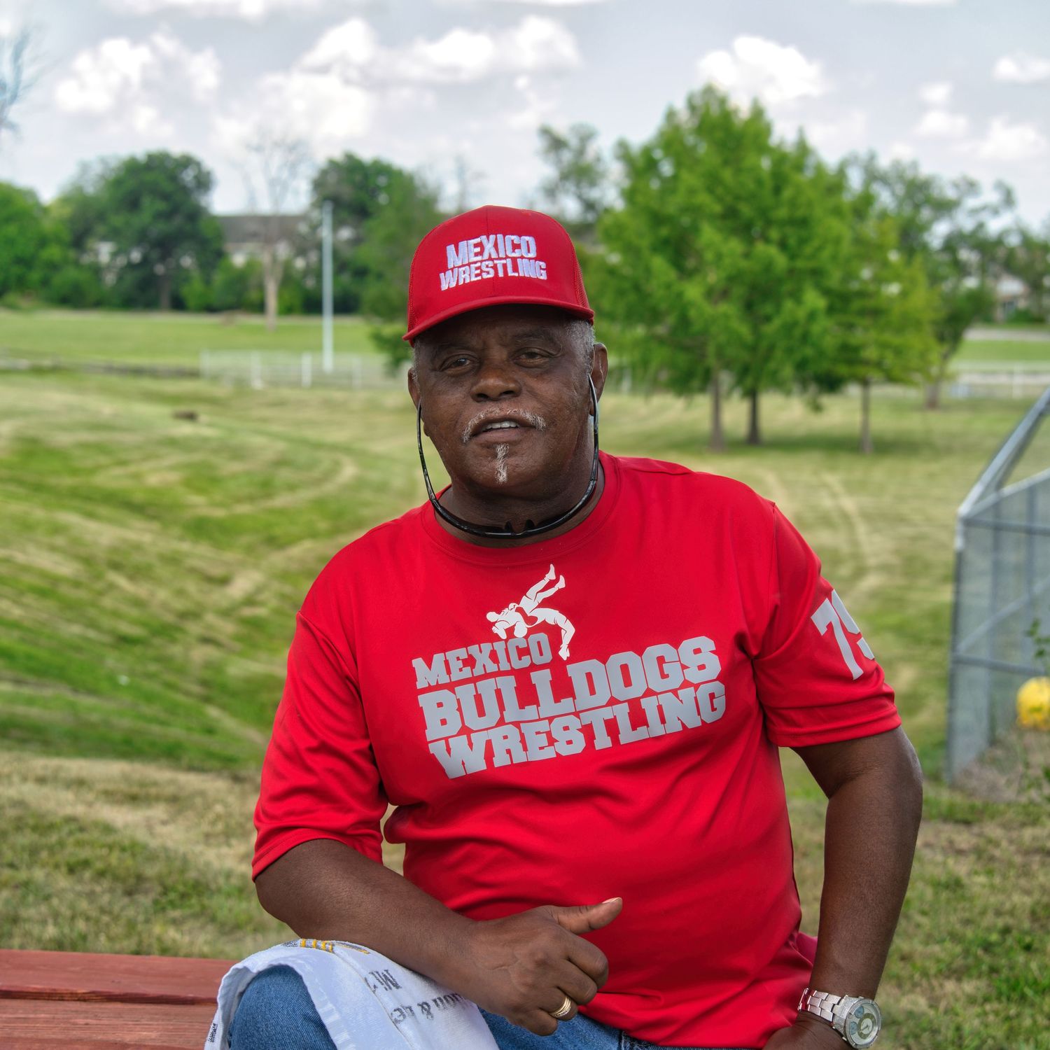 A man wearing a red hat and shirt with the text 'MERCER BULLDOGS WRESTLING' stands outdoors.