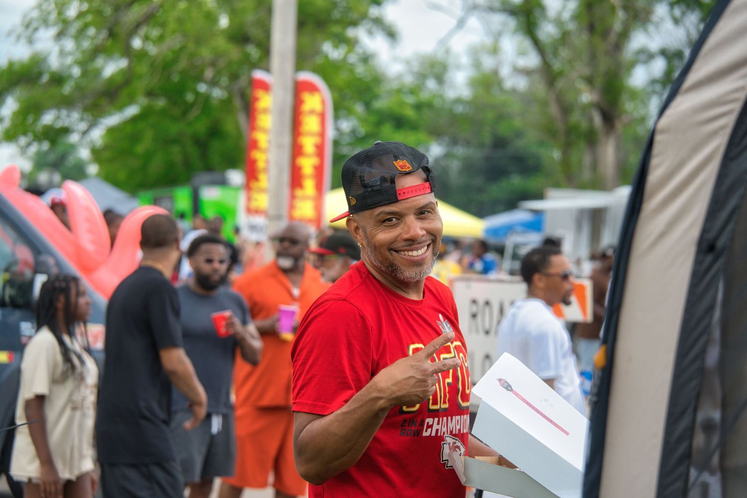 A smiling man in a red shirt is serving food from a mobile food truck.