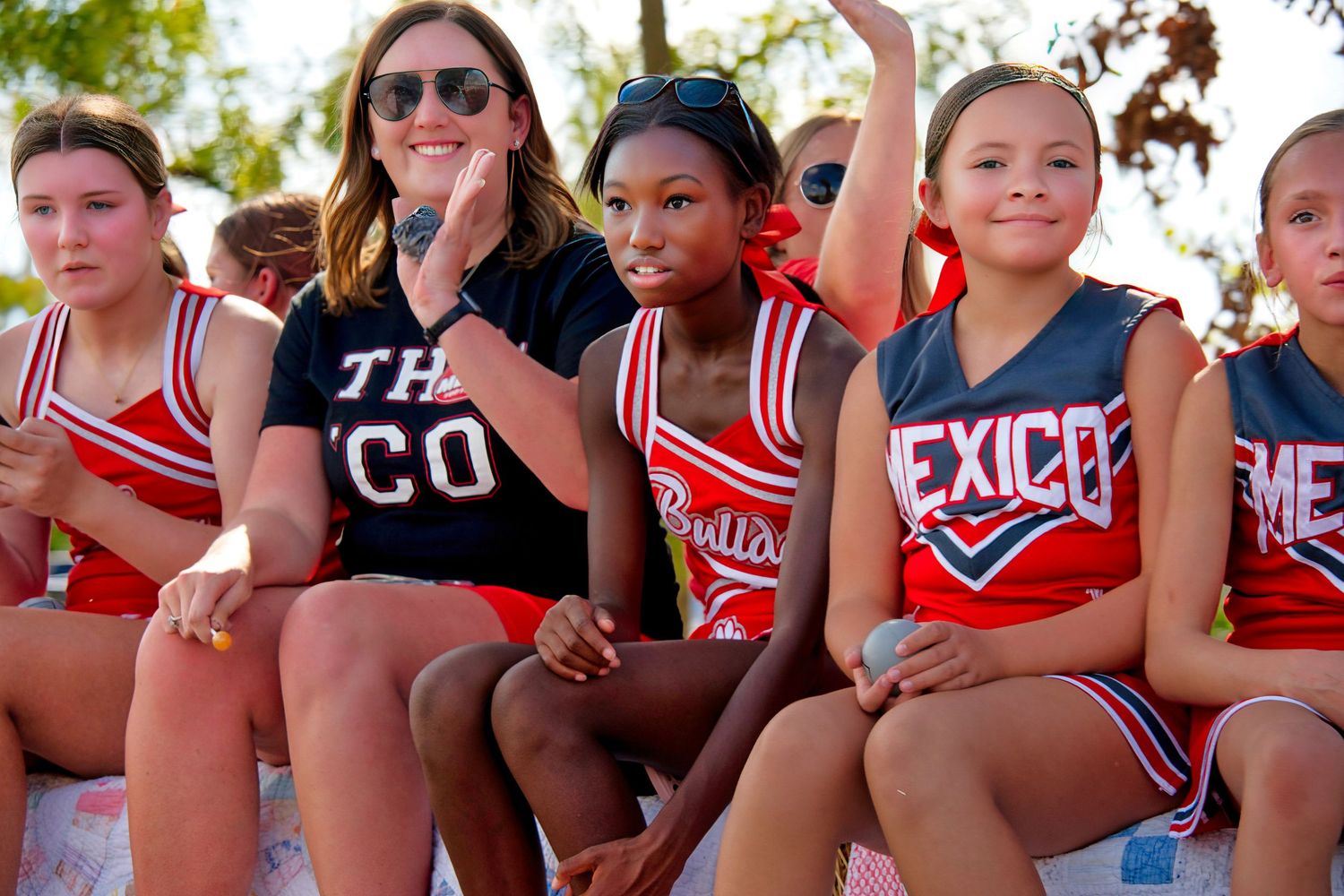 A group of young cheerleaders in red and white uniforms sitting on a bench.