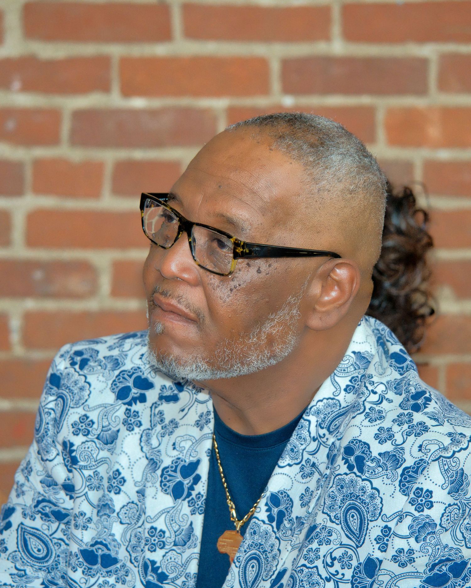 An older man with glasses and gray hair is wearing a blue and white patterned shirt and looking at the camera.