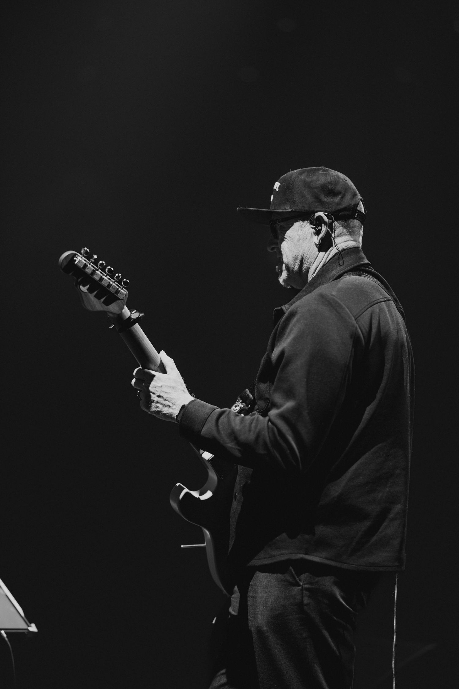 Black and white photo of a male guitarist performing on stage wearing a cap.