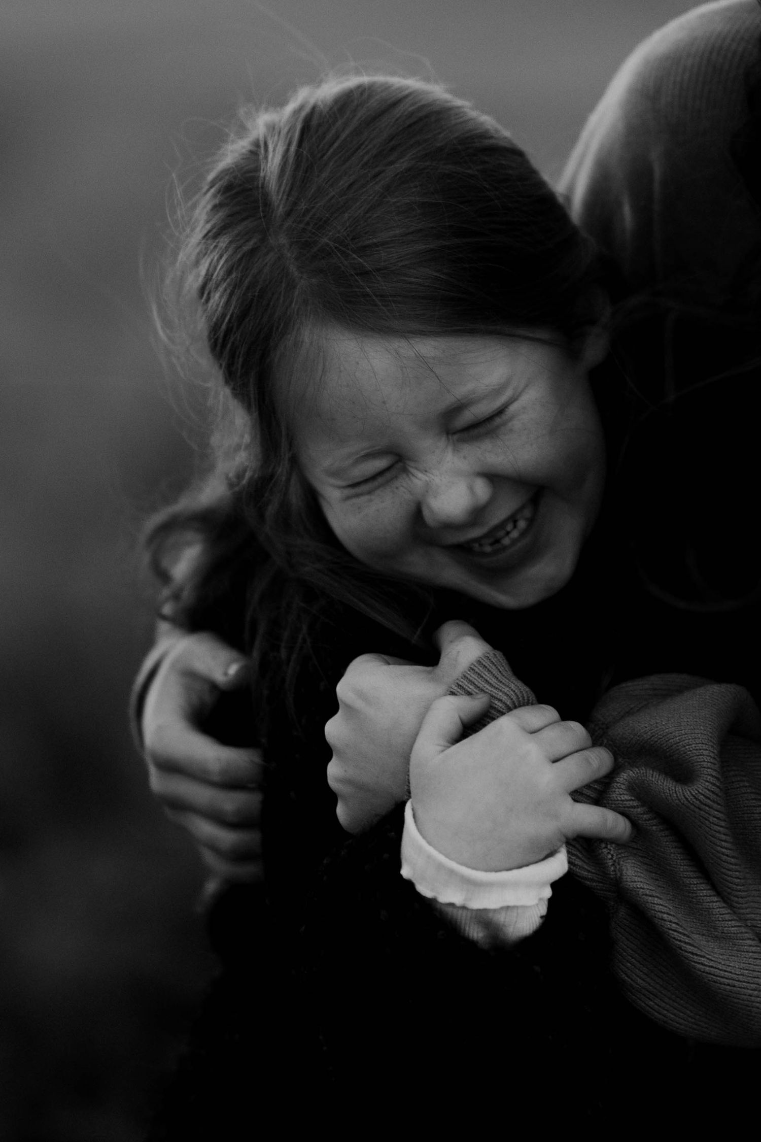 A laughing girl hugs someone tightly in a black and white portrait photo.