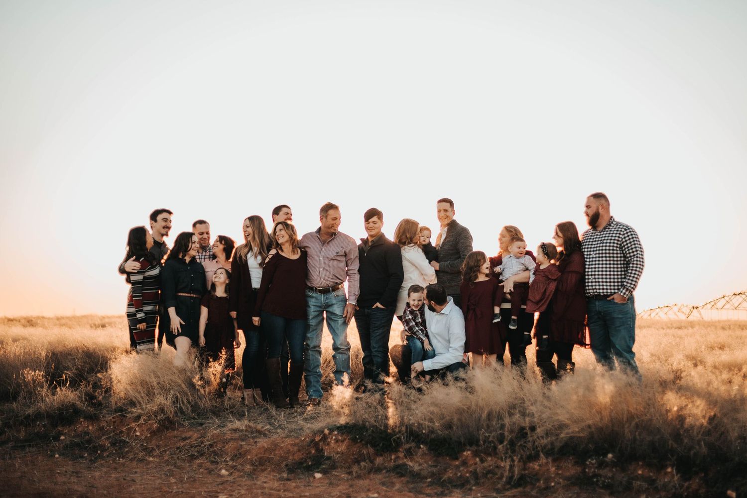 Extended family group portrait gathered together in open desert field during warm sunset light.