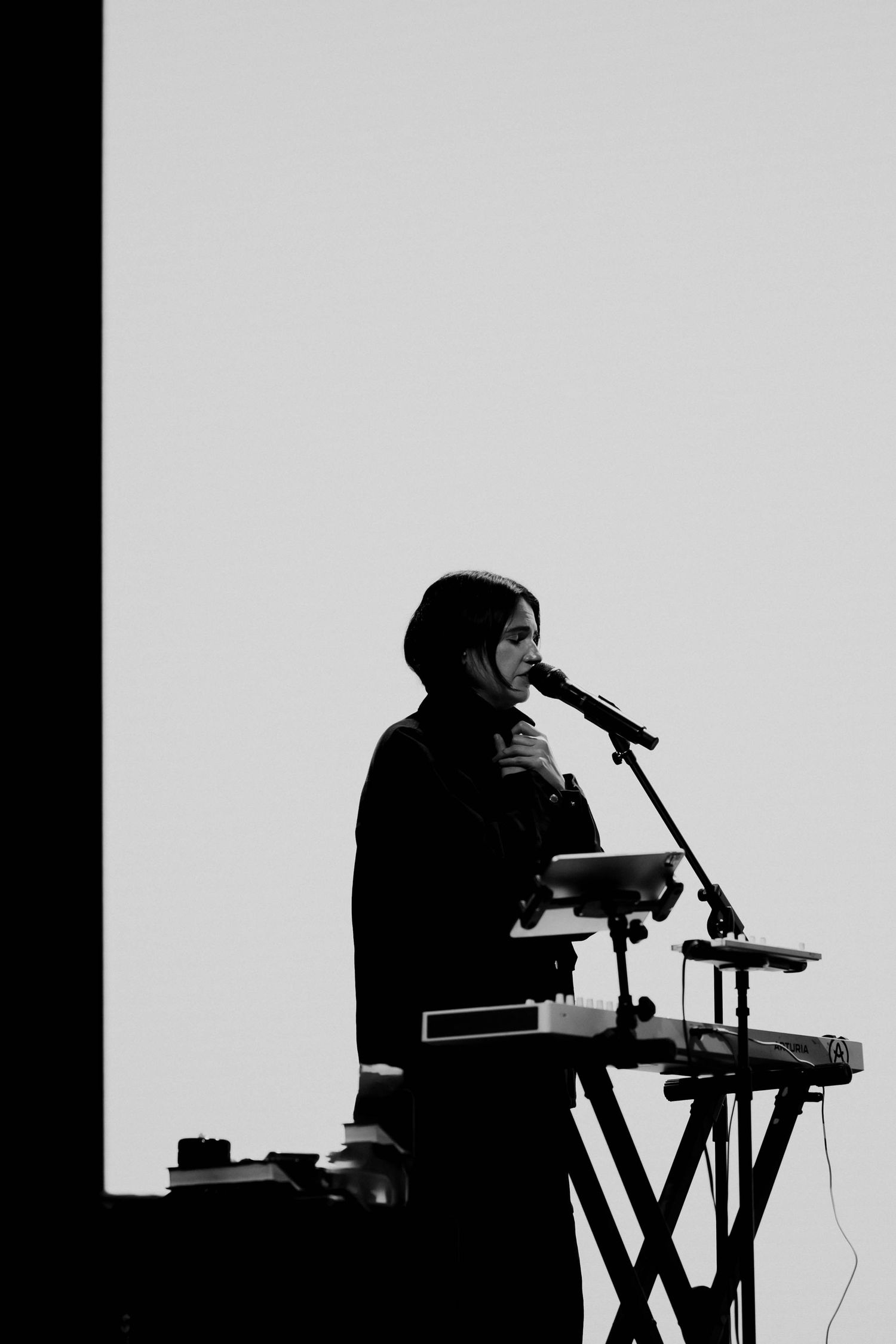 Silhouette of a musician performing at a keyboard and microphone on stage in black and white.