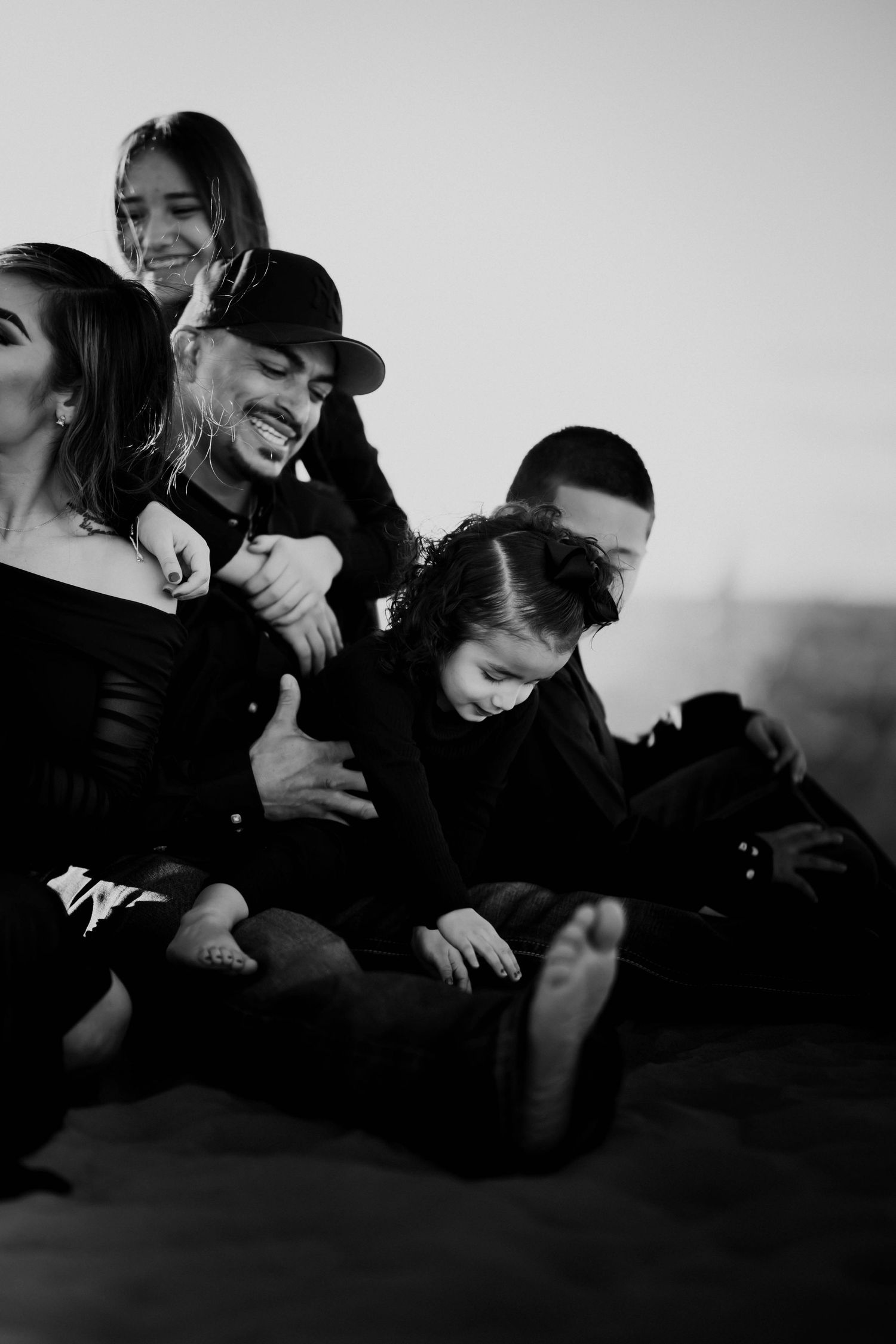 A black and white photo of a family laughing and relaxing together on sand dunes.