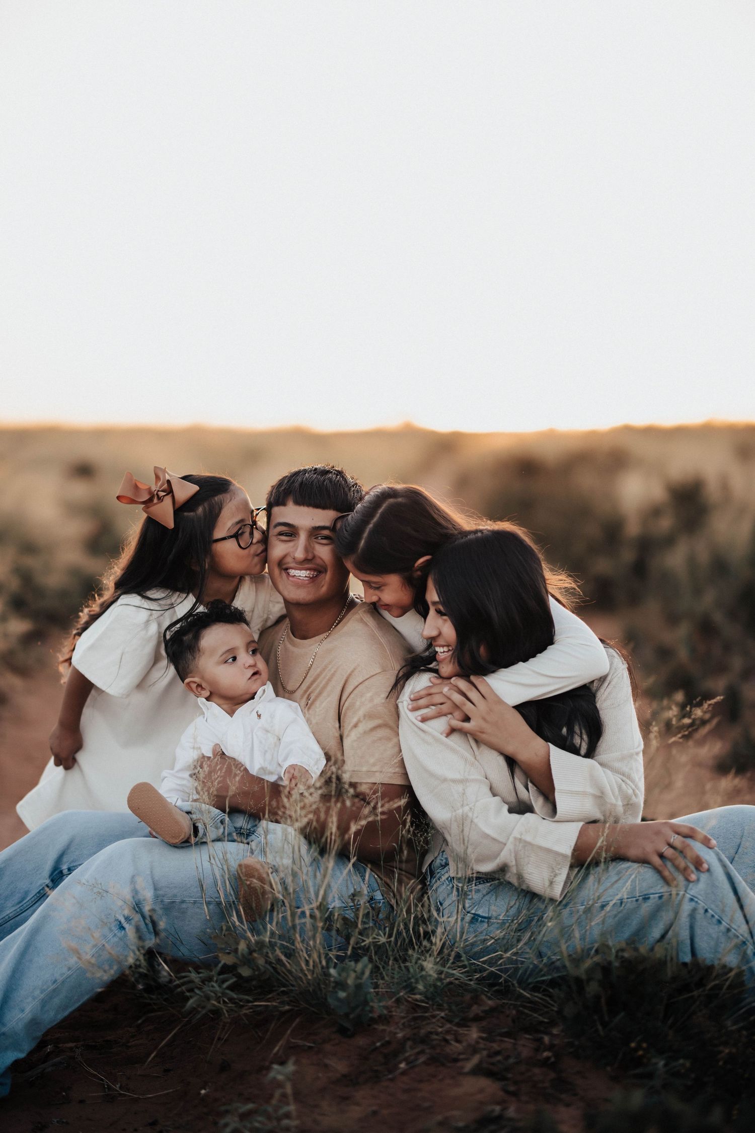 Happy family of five sitting together in a golden field at sunset.
