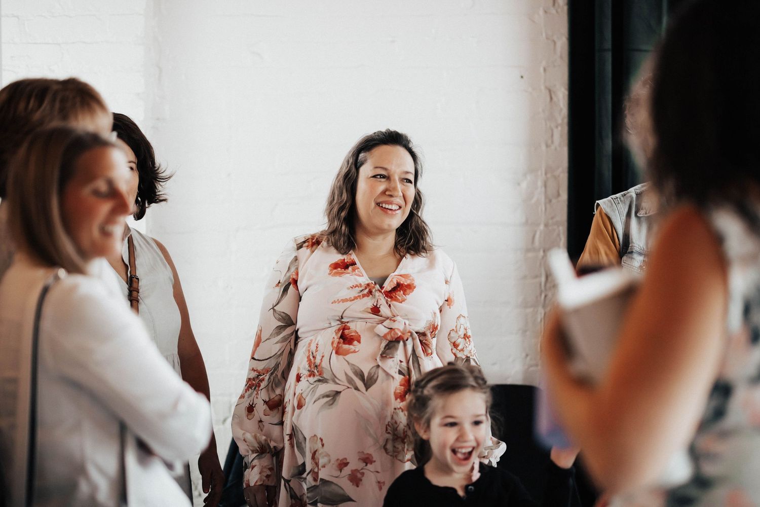 Pregnant woman in floral dress smiles warmly while socializing at a baby shower party.