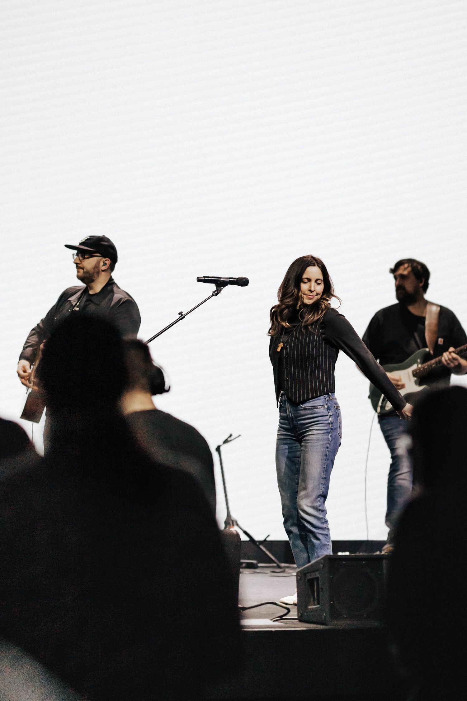 Female vocalist in striped top and jeans performing on stage with two guitarists before audience.