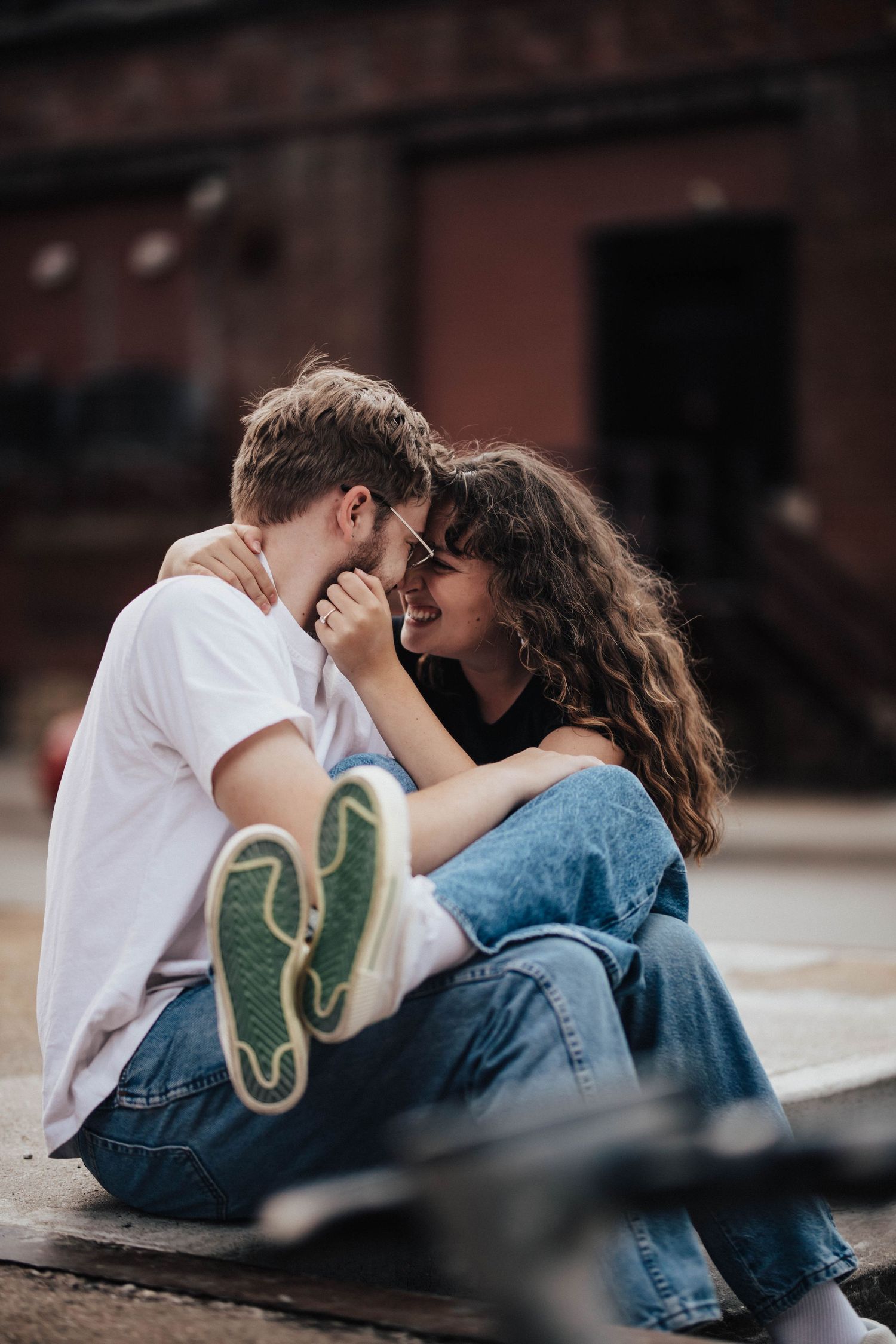 Young couple sitting outdoors, sharing a romantic moment, smiling and embracing on a city street.