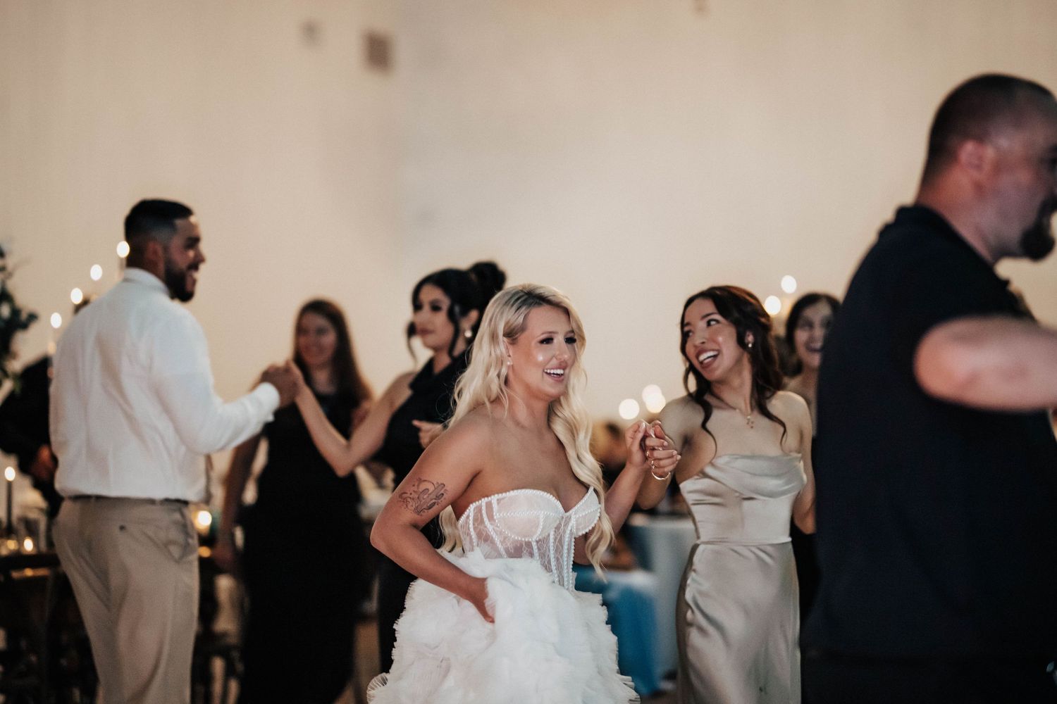 Smiling bride in strapless gown celebrates with guests at lively wedding reception.