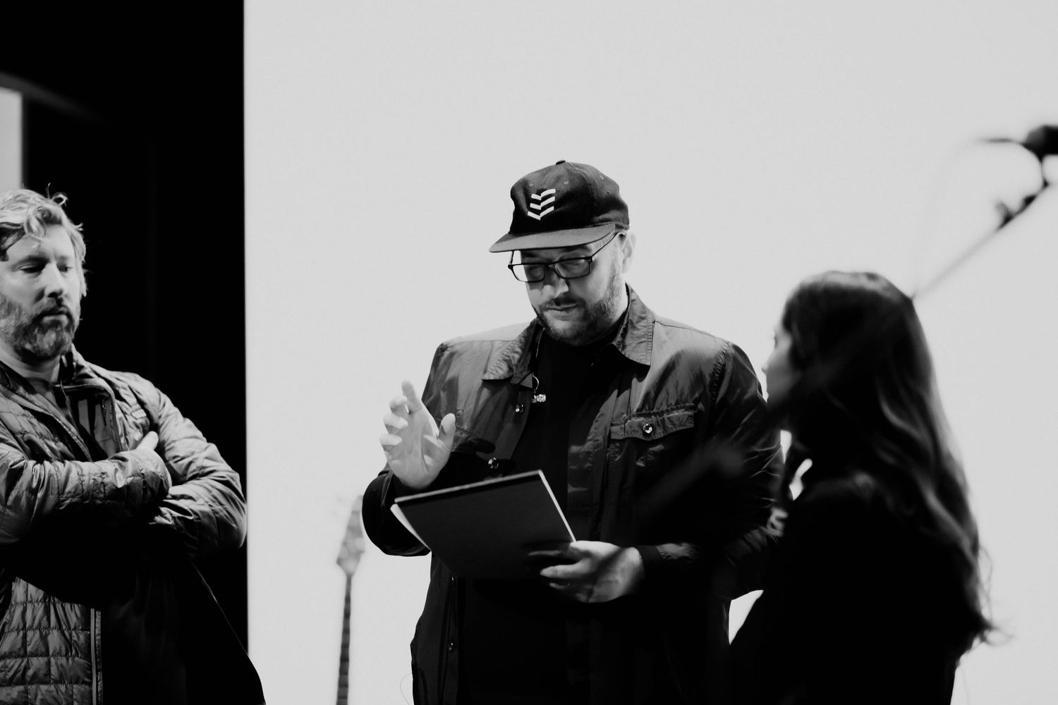 Black and white photo of three people reviewing documents on a film set indoors.