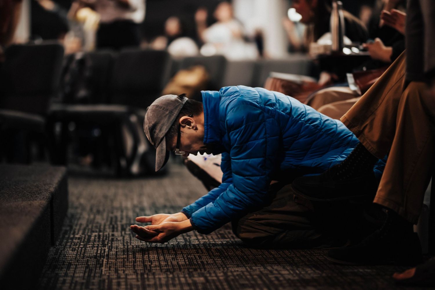 A man in a blue jacket kneels in prayer on the floor during a church service.