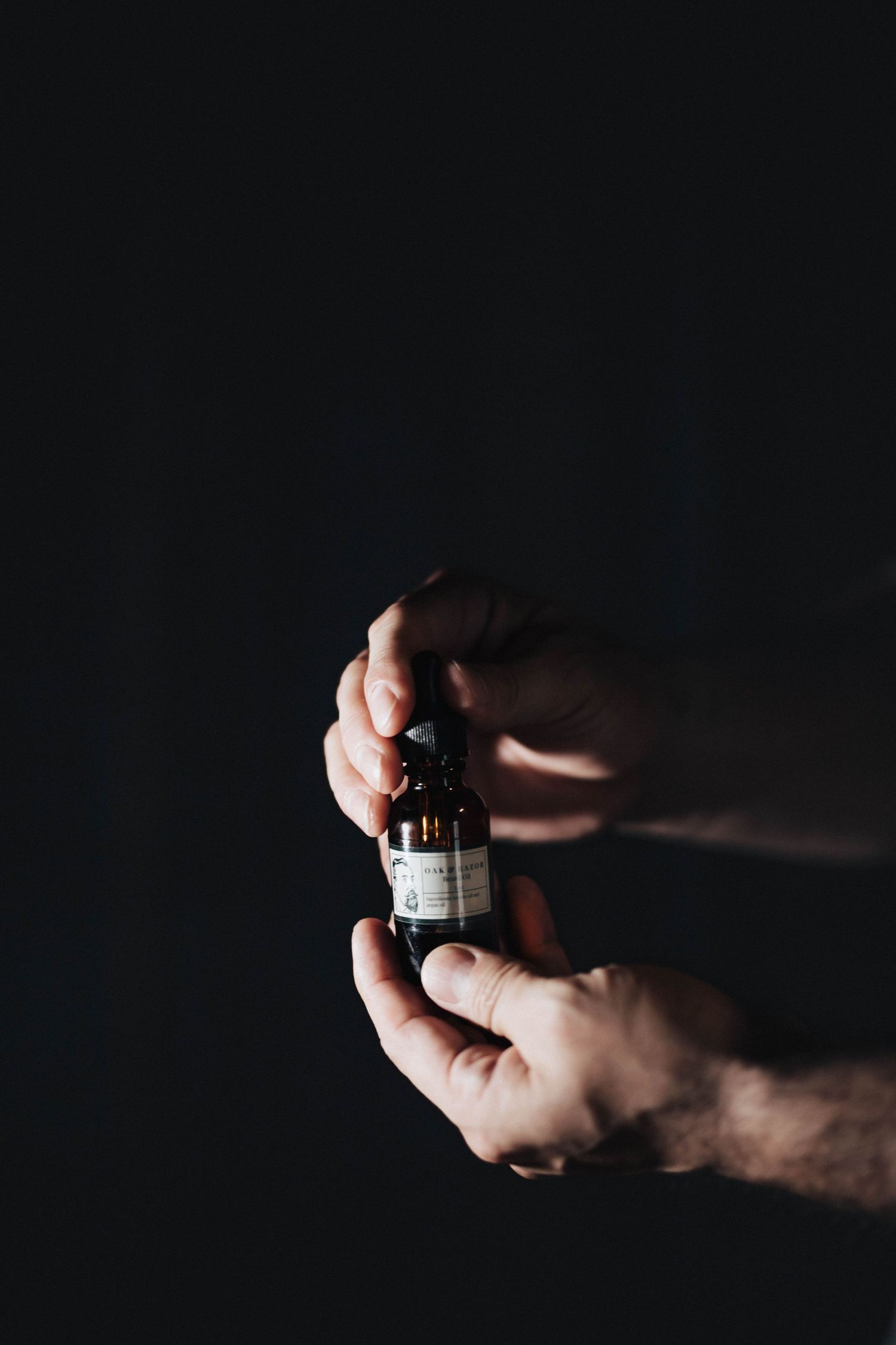 Close-up of hands holding a small dark glass bottle against a black background.
