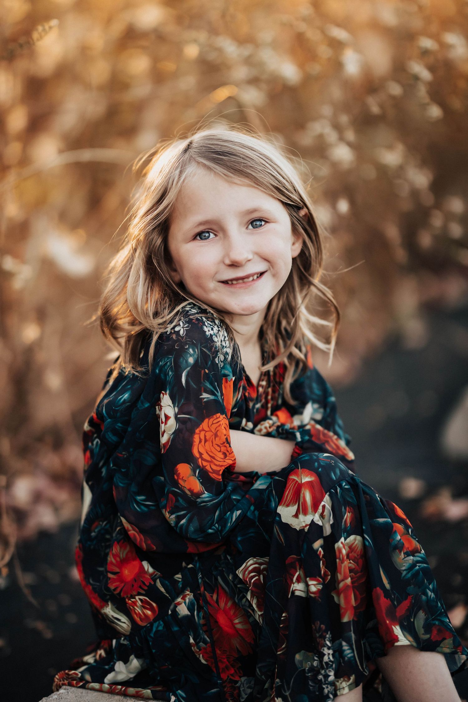 Happy young girl in floral dress smiling during golden autumn outdoor portrait session.