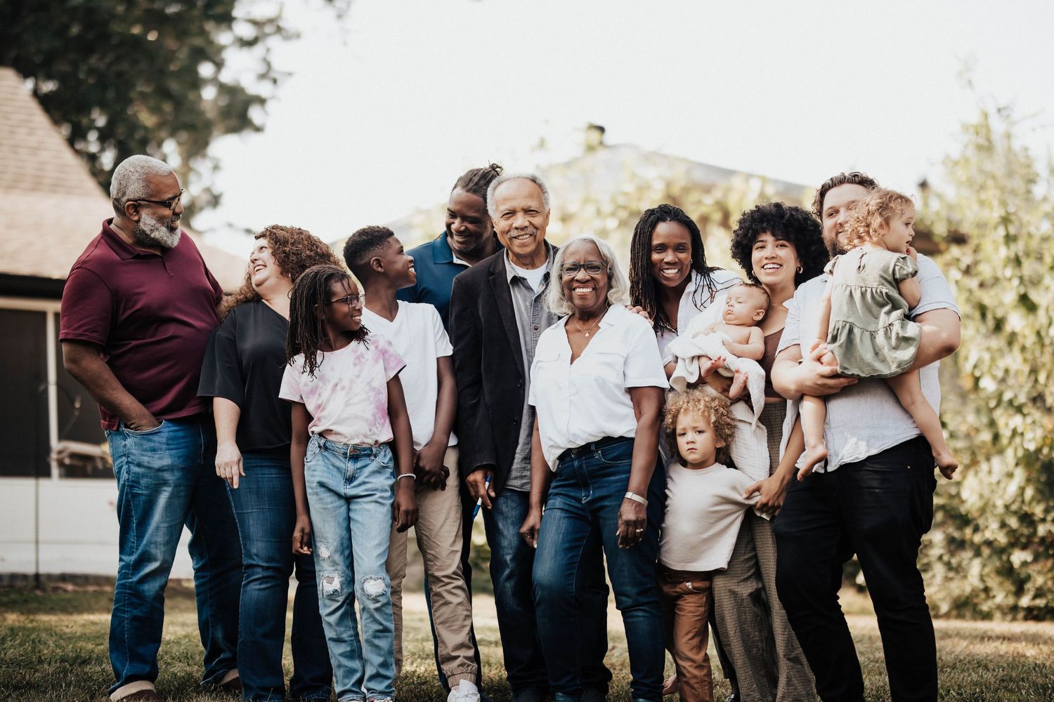 Large multigenerational Black family smiling together outdoors in backyard.
