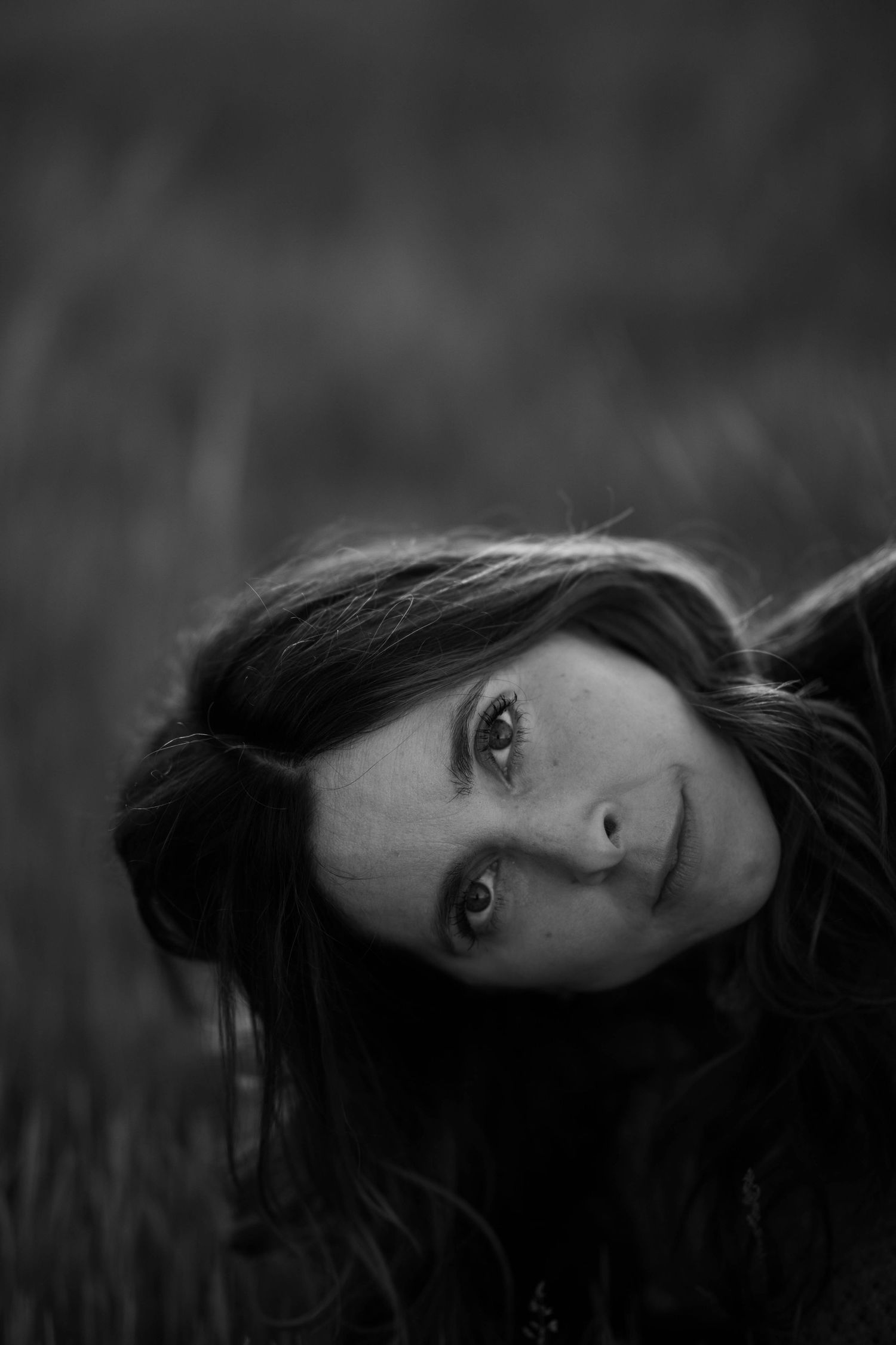 Black and white portrait of a young woman lying in grass looking up at the camera.