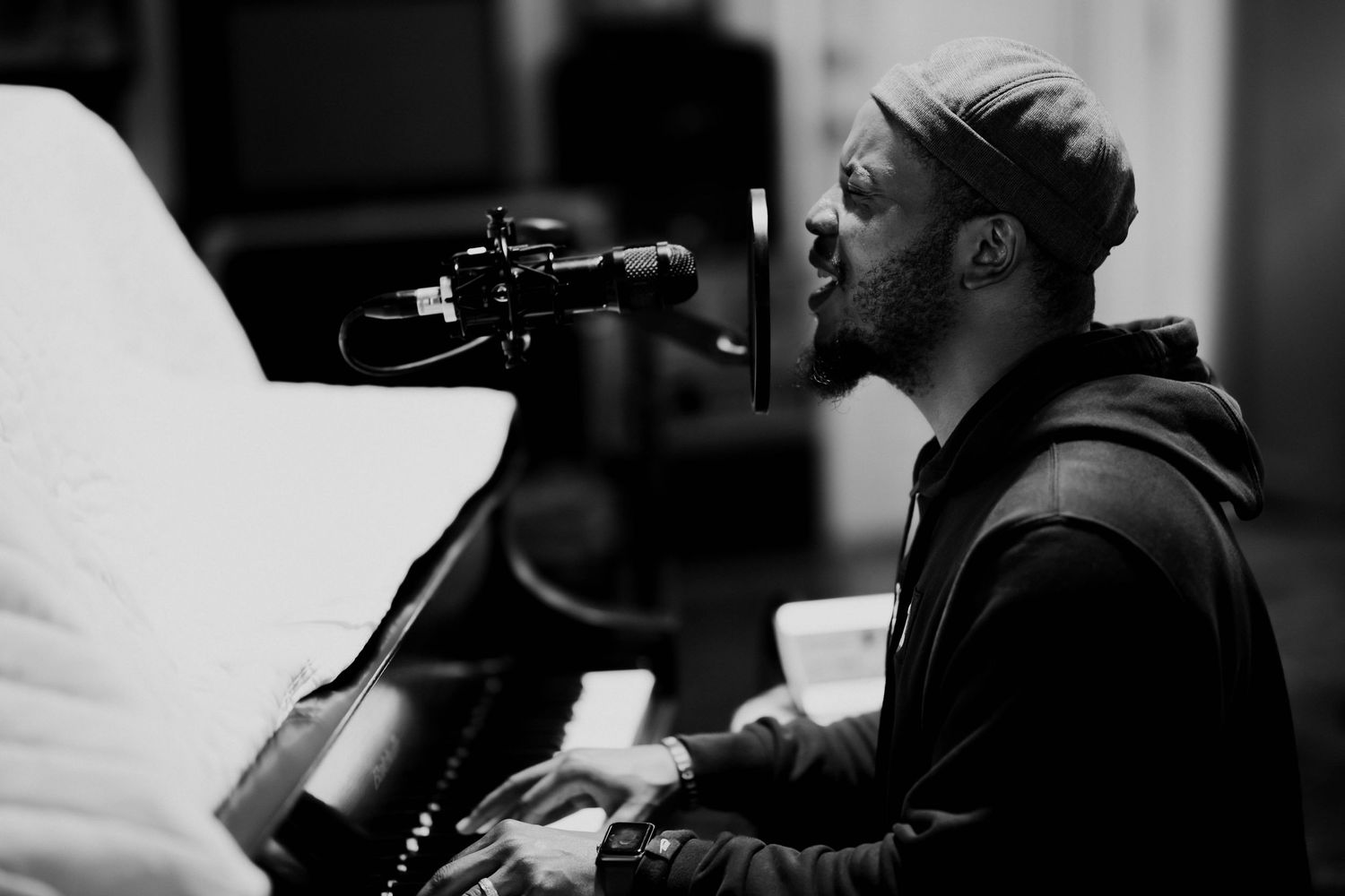 Black and white photo of a musician singing and playing piano in a recording studio.