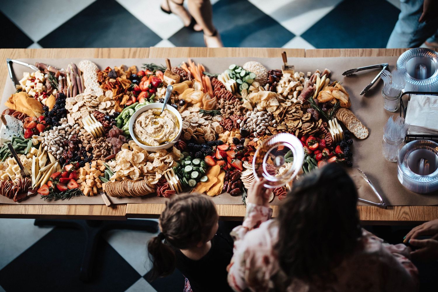 An overhead view of guests gathered around a large elaborate charcuterie grazing board at a baby shower.